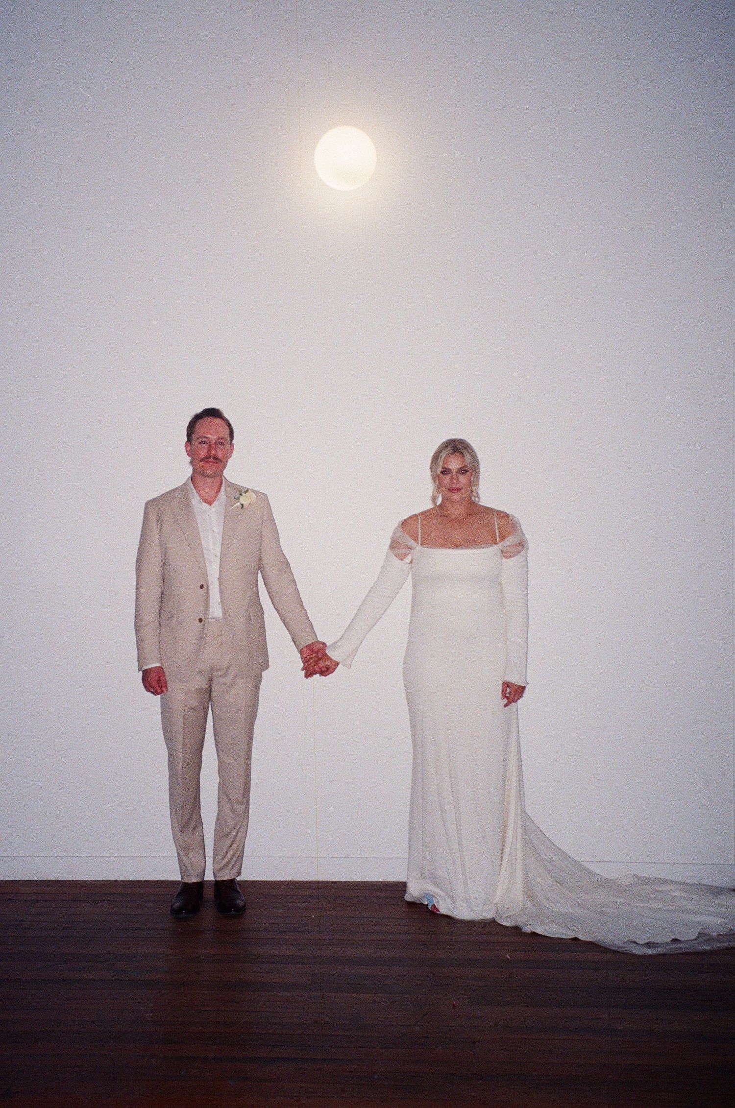 Couple stands together against white wall with full moon visible in background.