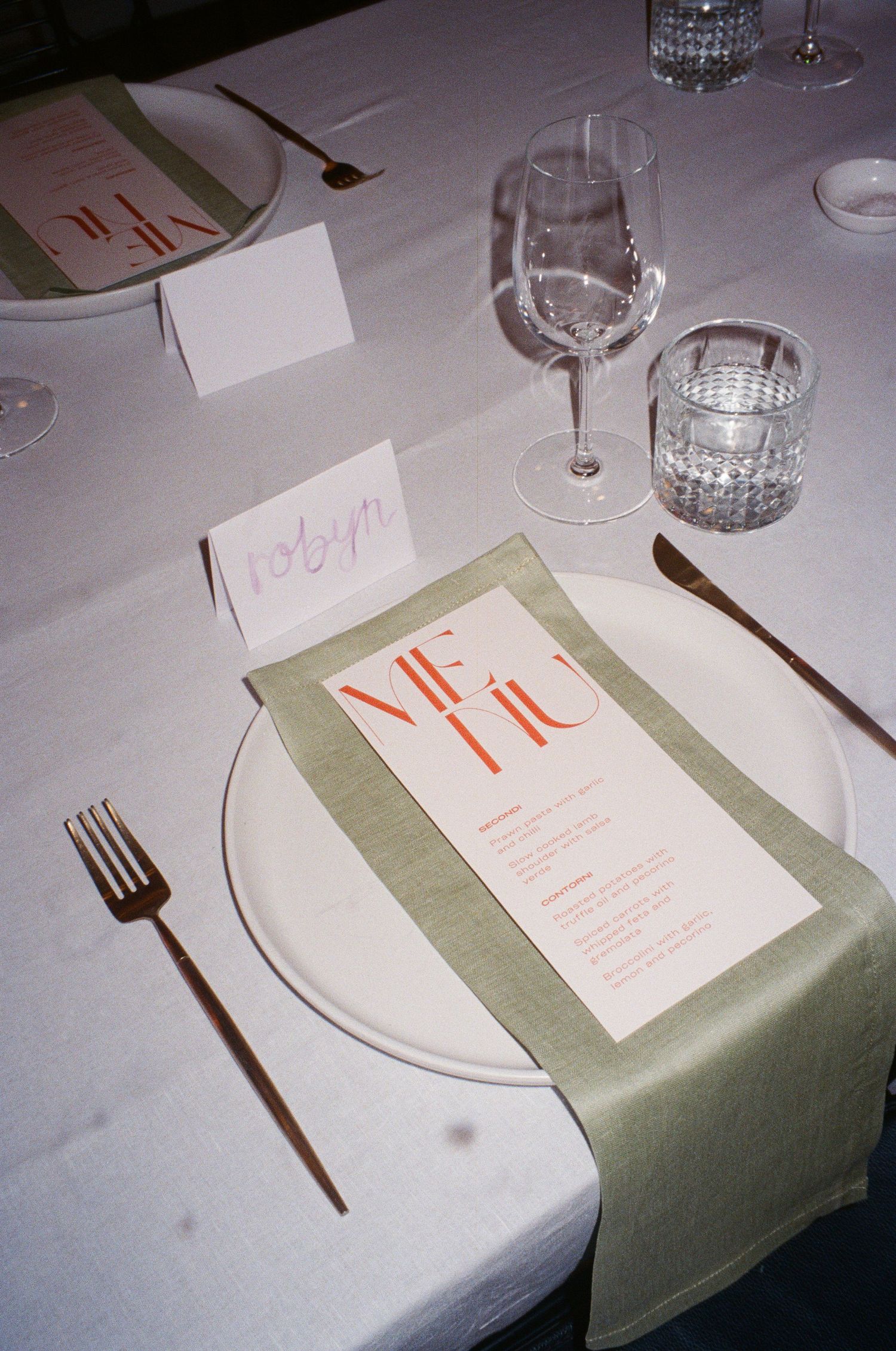 Wedding place setting with white plate, sage green napkin, and modern menu card.
