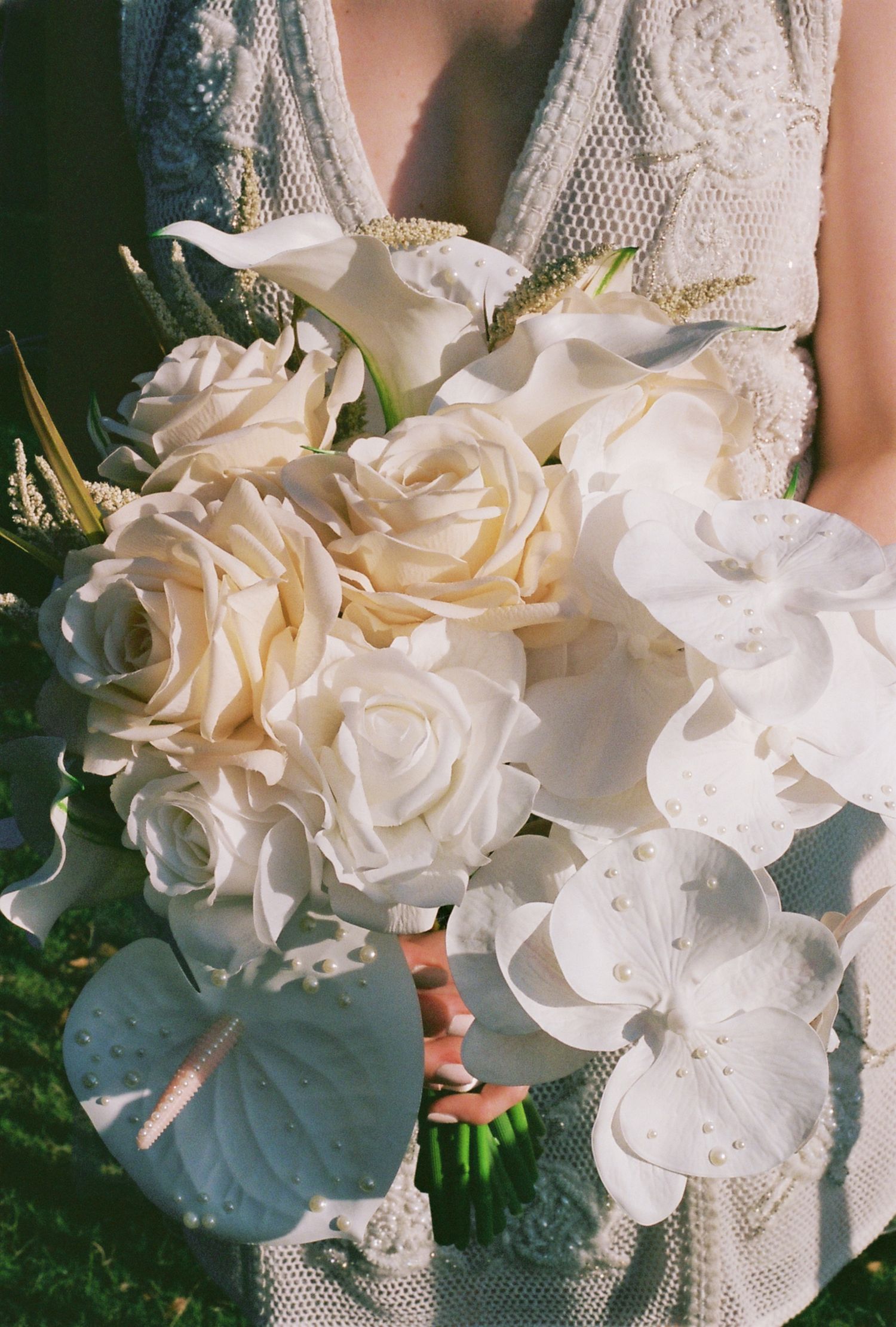 An elegant bridal bouquet featuring white roses and orchids against lace details.