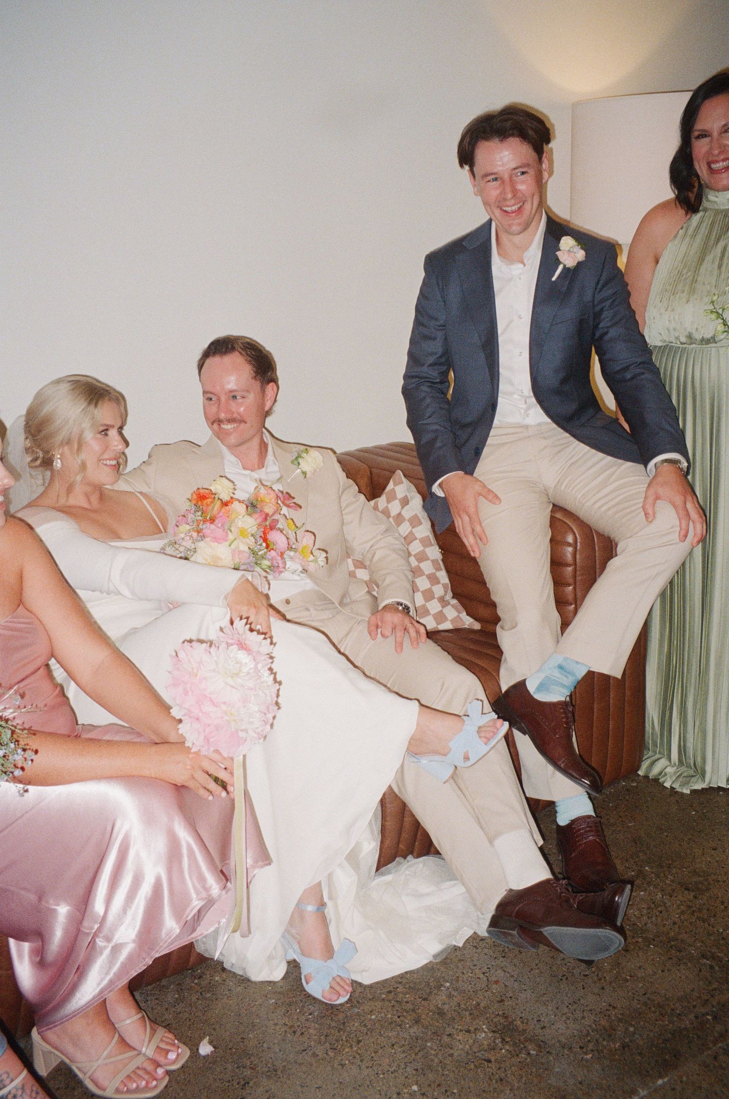 Wedding party members relaxing on a couch in formal attire during reception festivities.