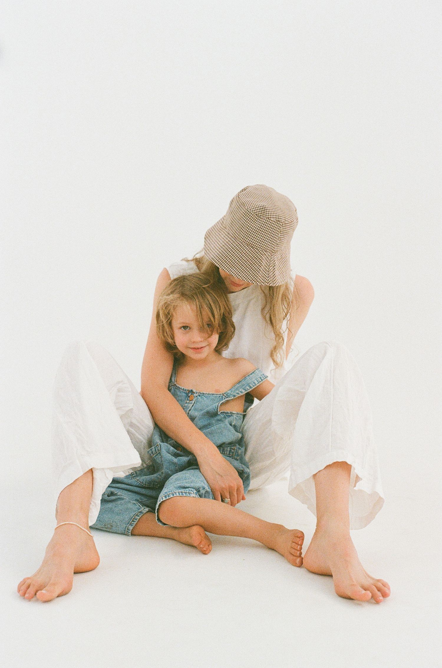 Two people in casual attire sitting closely together on white background.