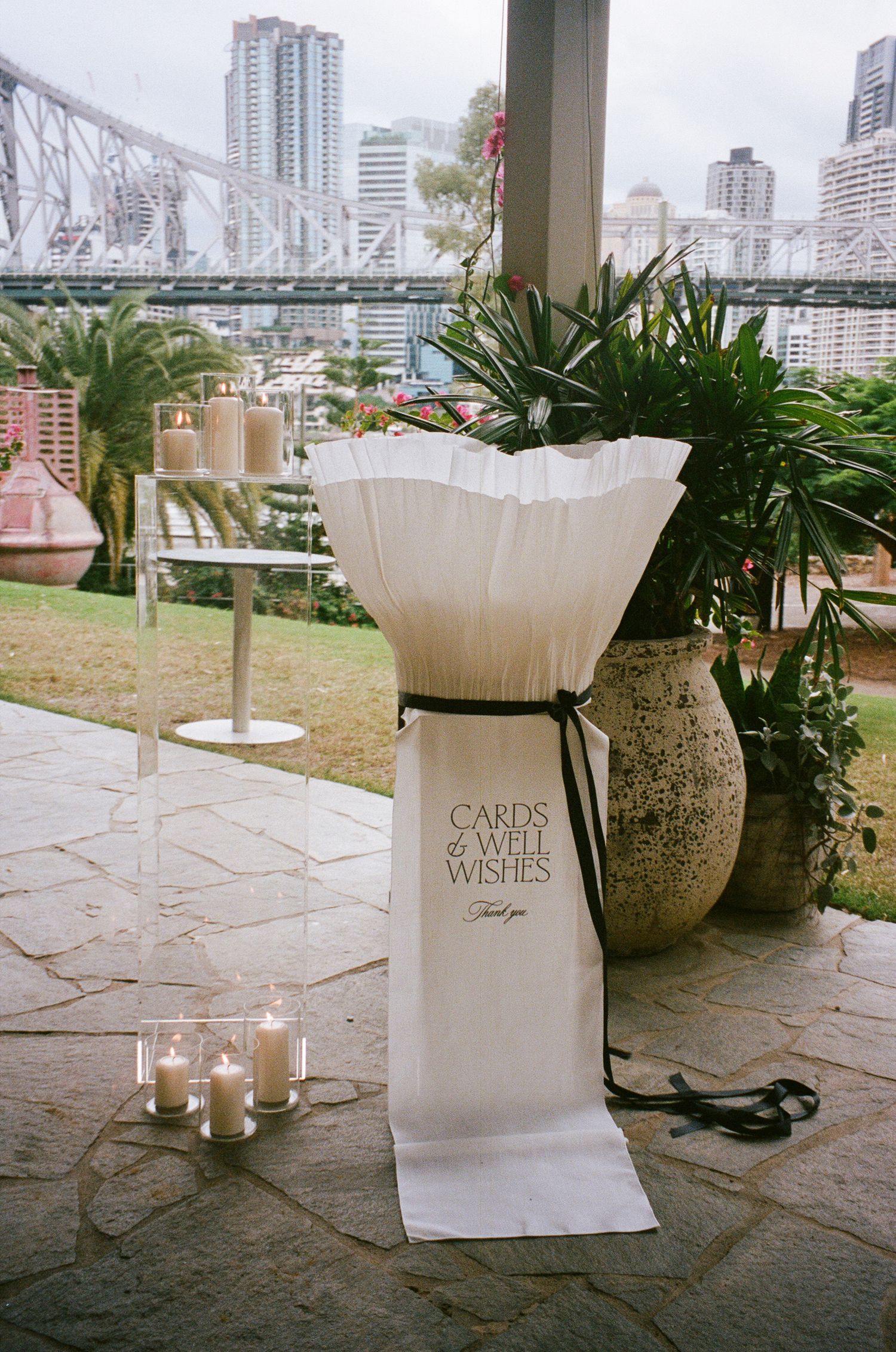 Elegant outdoor wedding reception setup with white card boxes and candles overlooking a city skyline.