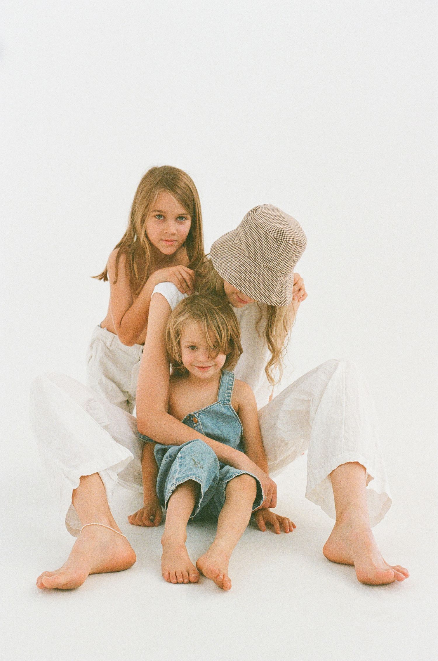 Artistic studio portrait of three people in white clothing sitting closely together.