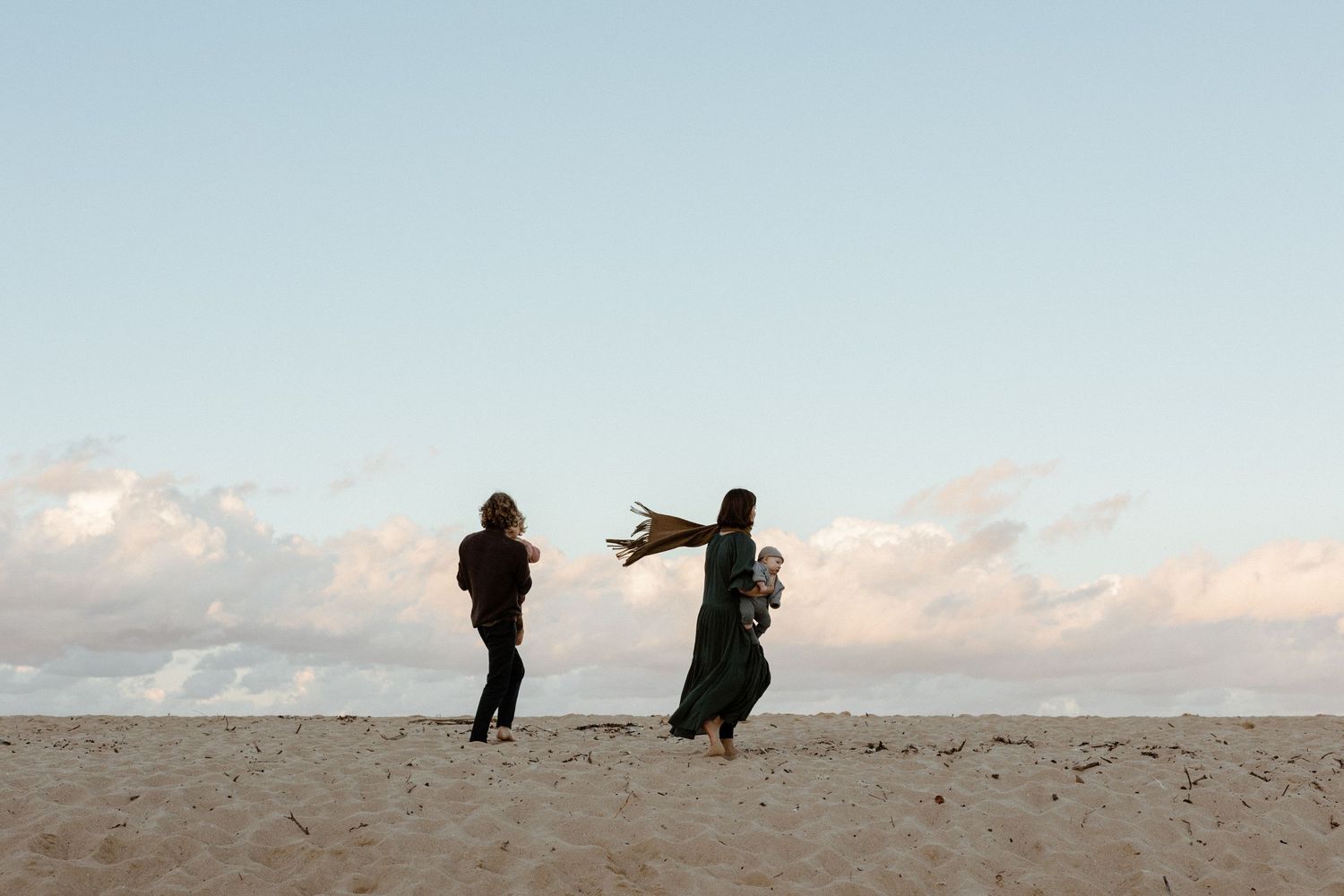 Two silhouettes playing and reaching toward each other on sandy beach at dusk.