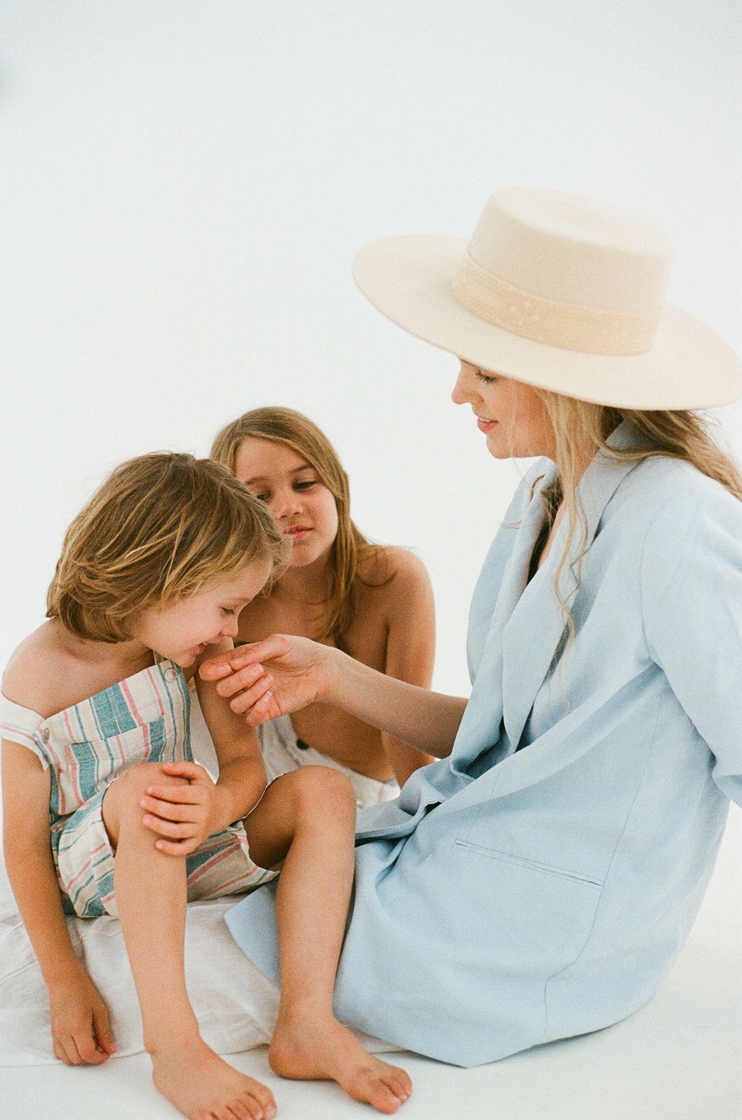 Group sitting together on white backdrop, one wearing light blue dress and beige sun hat.