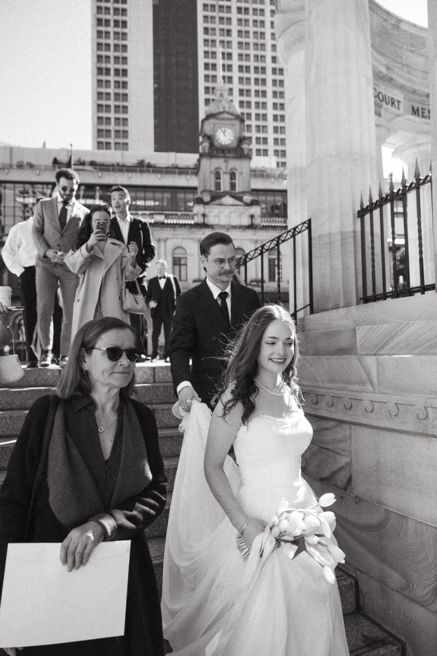 A wedding party walks together outside a building with classical architecture in black and white film.