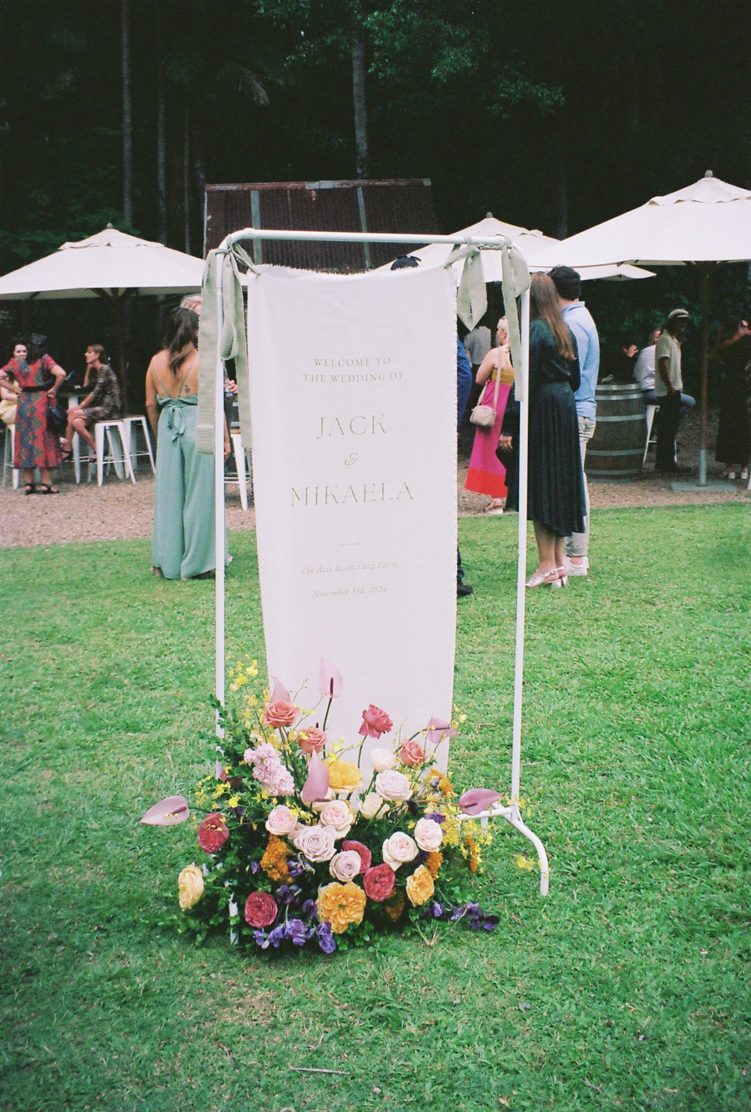 A decorative wedding welcome sign with floral arrangements on a grass lawn.