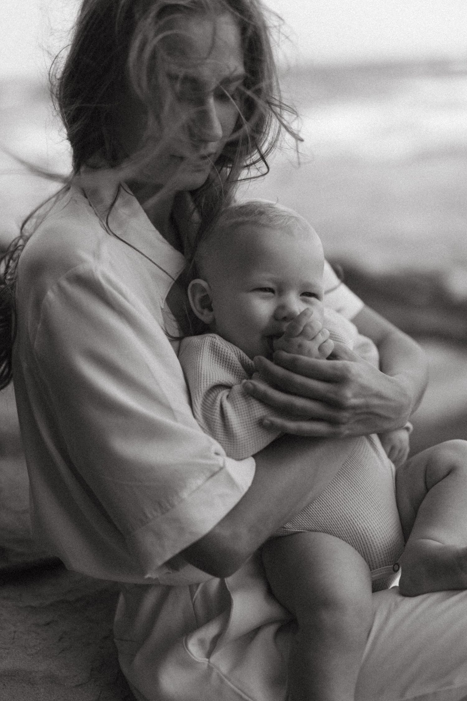 Black and white portrait of parent cradling smiling baby outdoors.