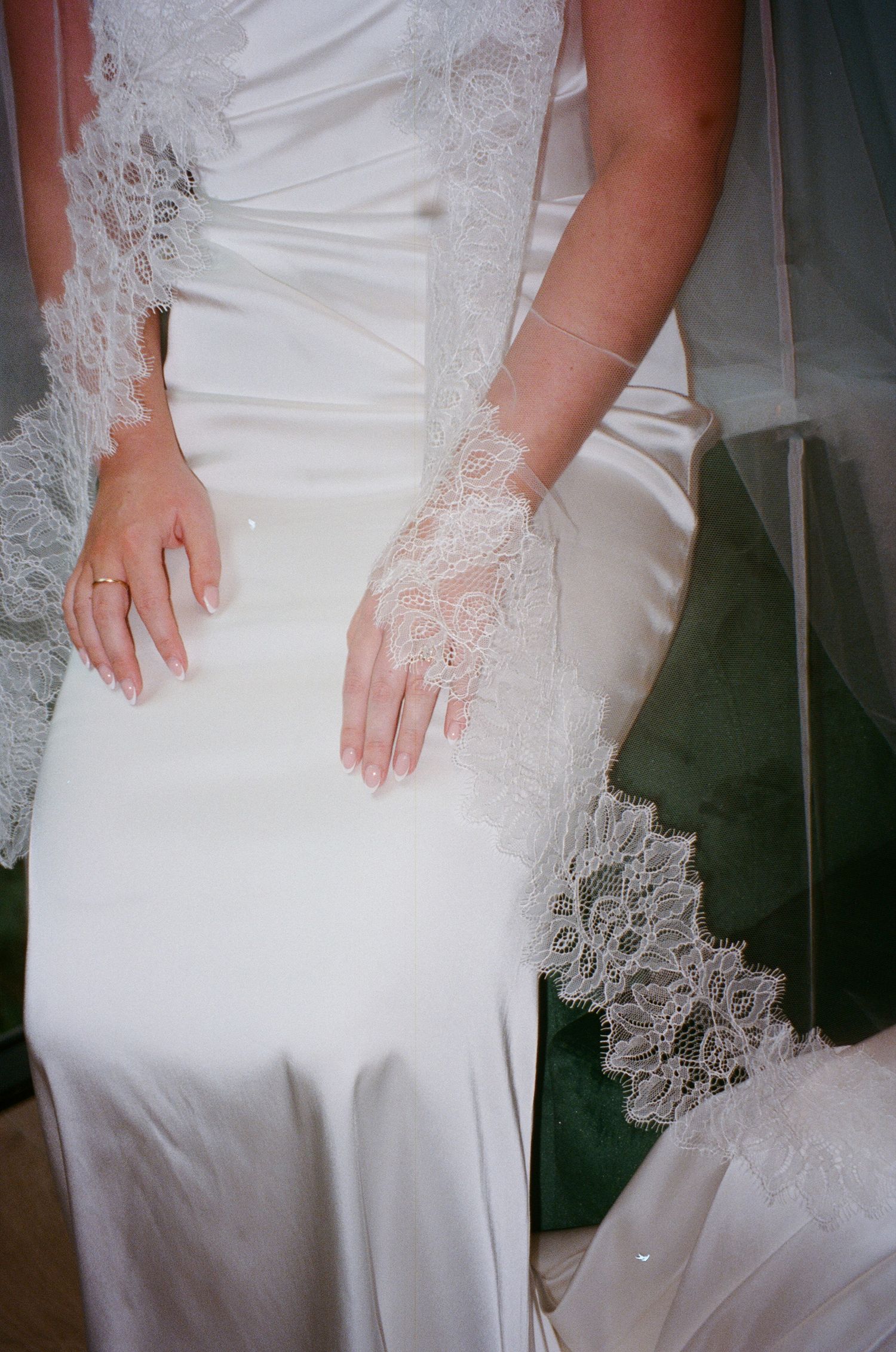 Detail shot of a white lace-trimmed wedding dress showing delicate lacework on sleeves and hem against dark background.