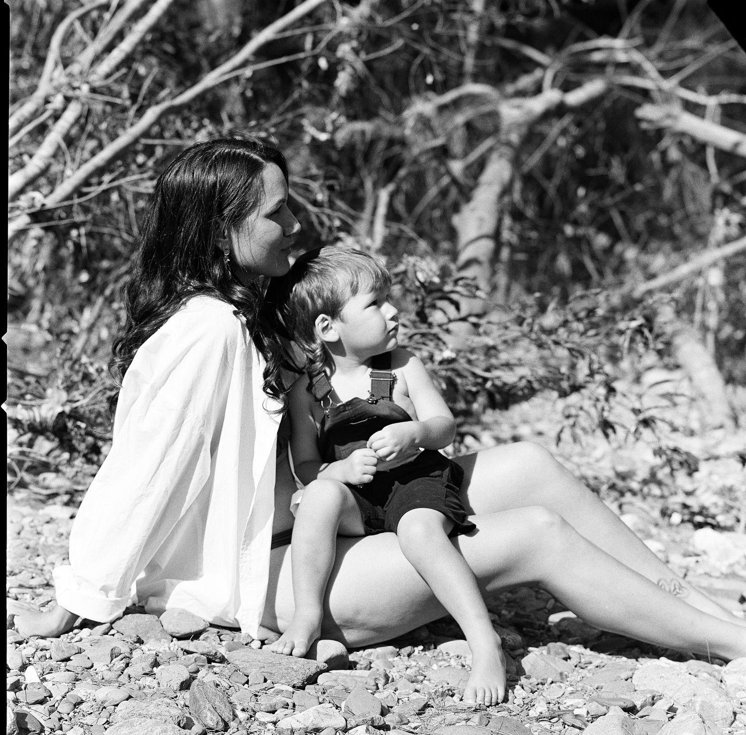 Black and white photo of a parent and child sitting together outdoors in nature.