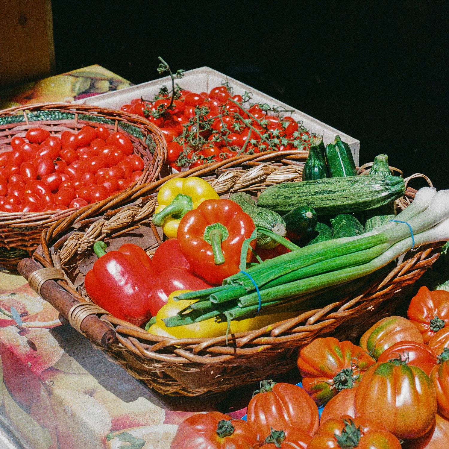 Fresh produce display with colorful tomatoes, peppers and green vegetables in woven baskets.