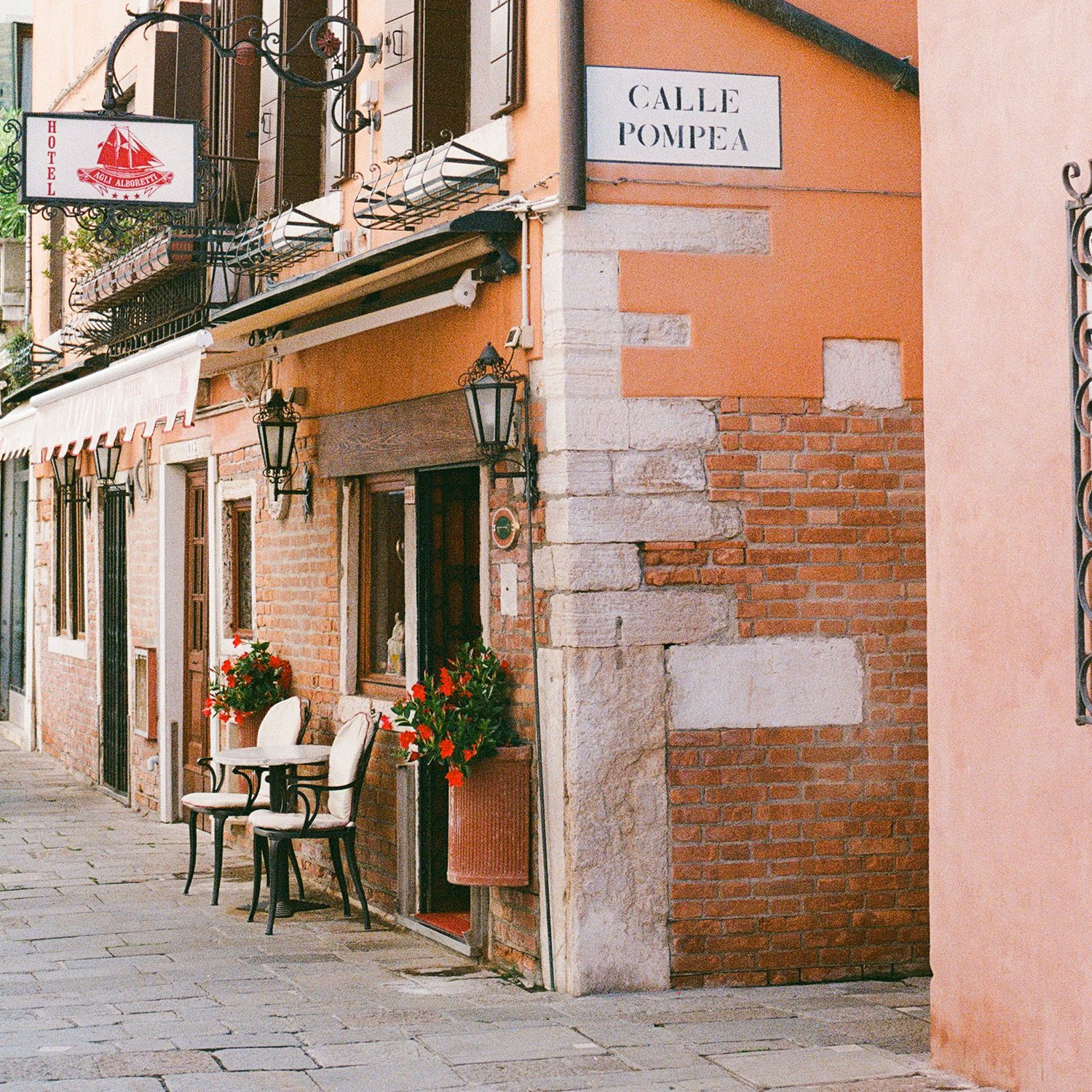Charming Italian street corner with orange walls, vintage lanterns and outdoor cafe seating.