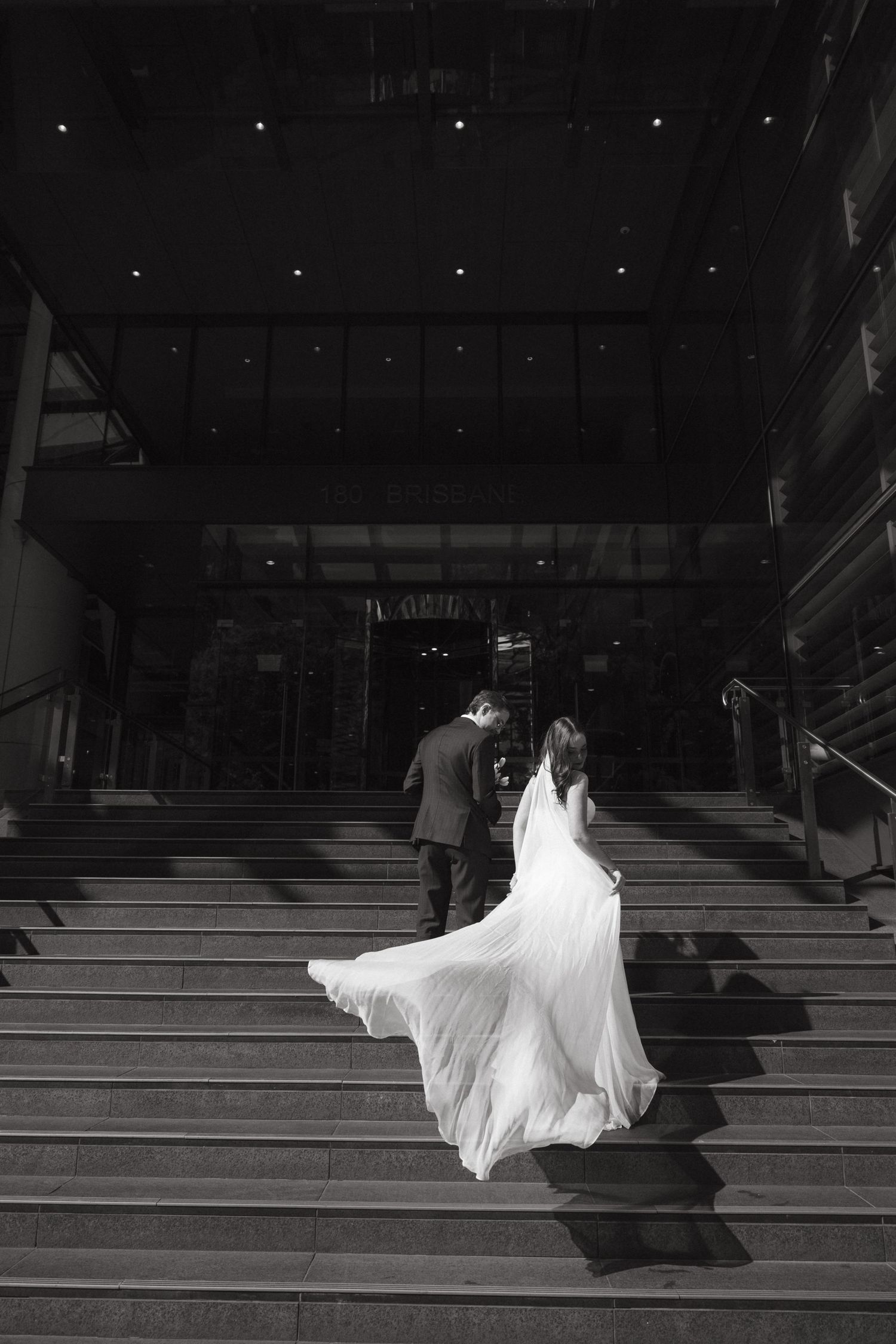 A bride in a flowing white wedding dress descends dramatic stone steps in a black and white sequence of photos.