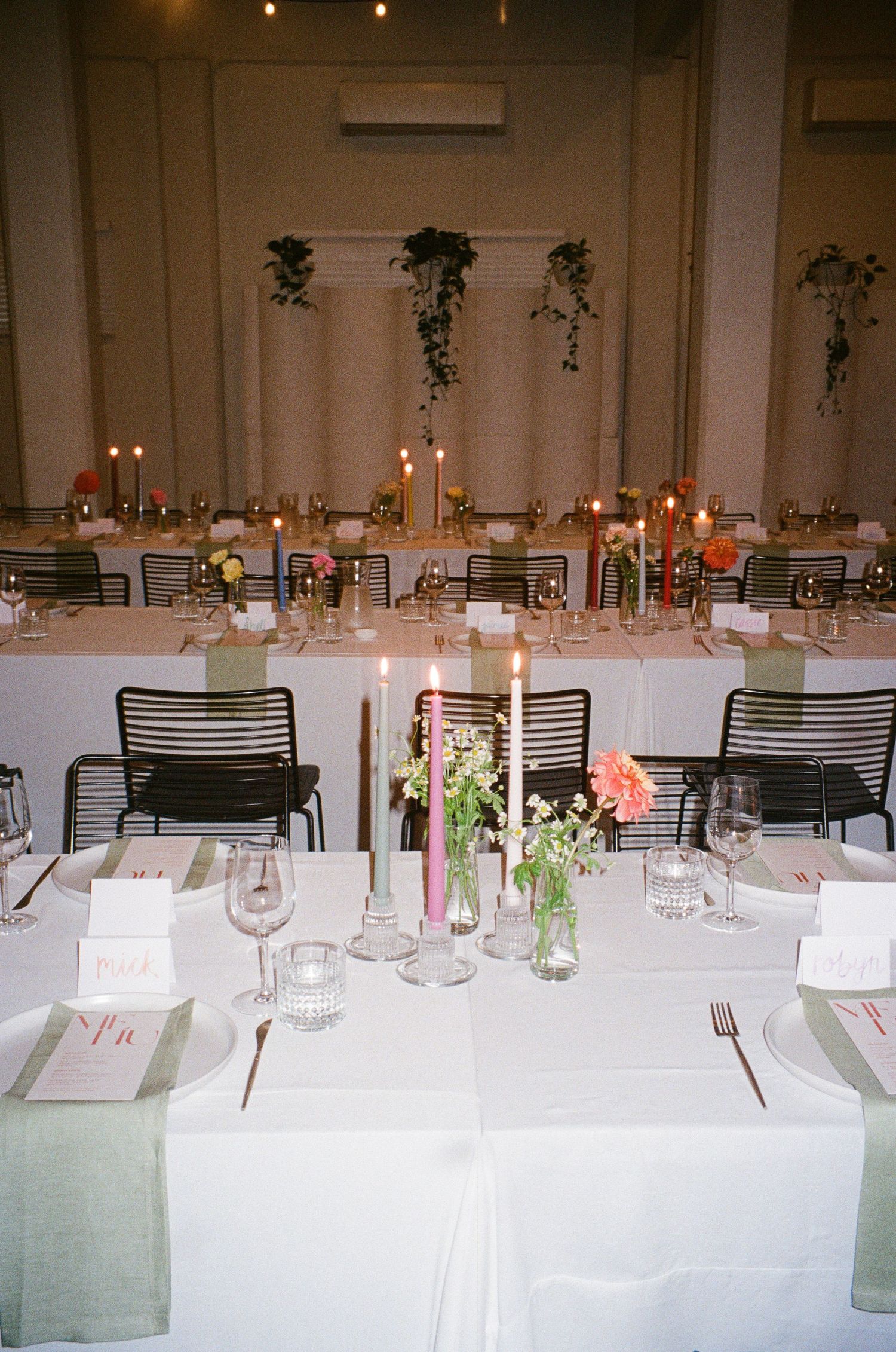 Elegant wedding reception table setting with candles, flowers, and hanging greenery.