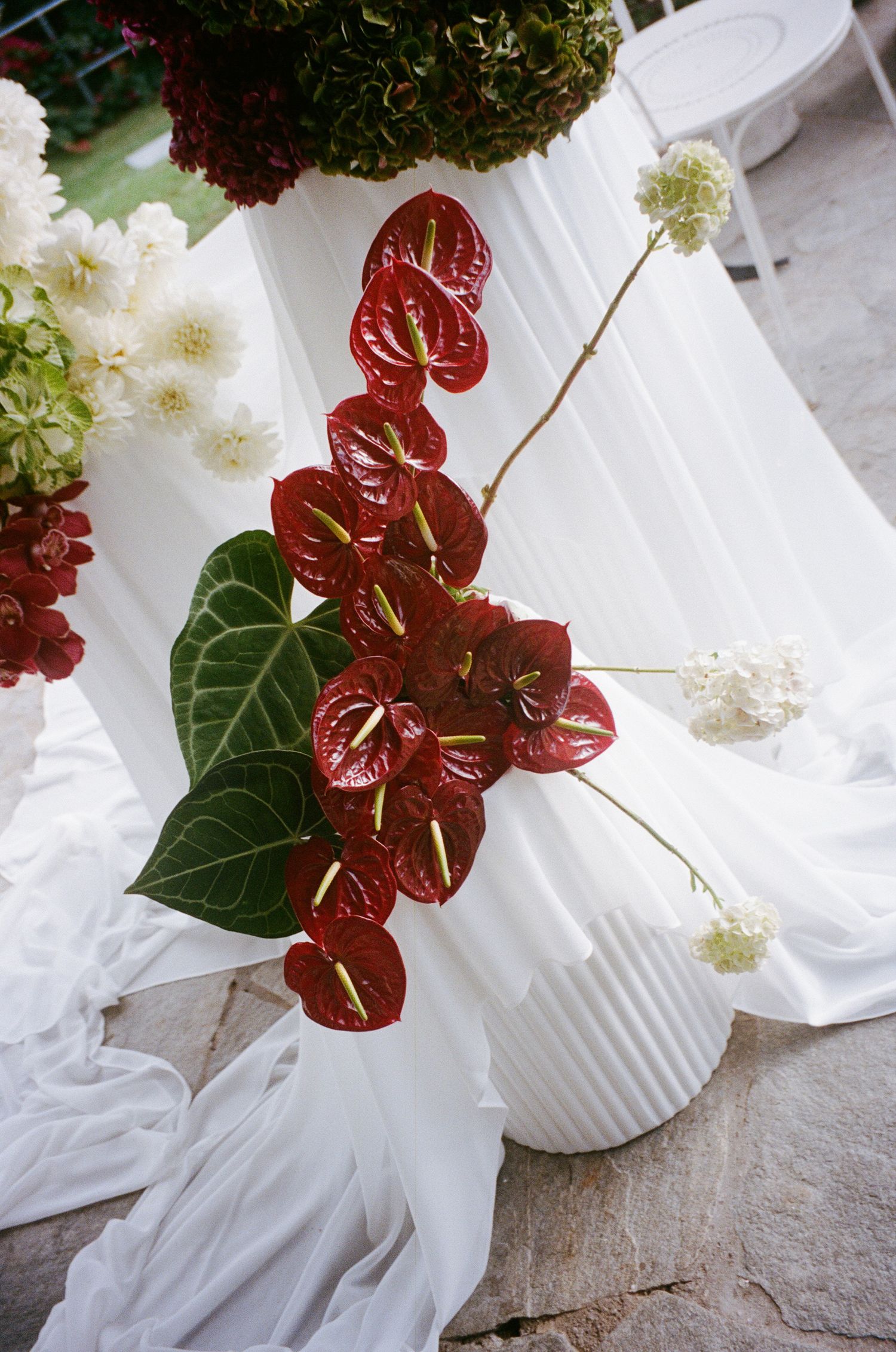 White floral arrangements with red anthurium flowers in ribbed vases on a textured surface.