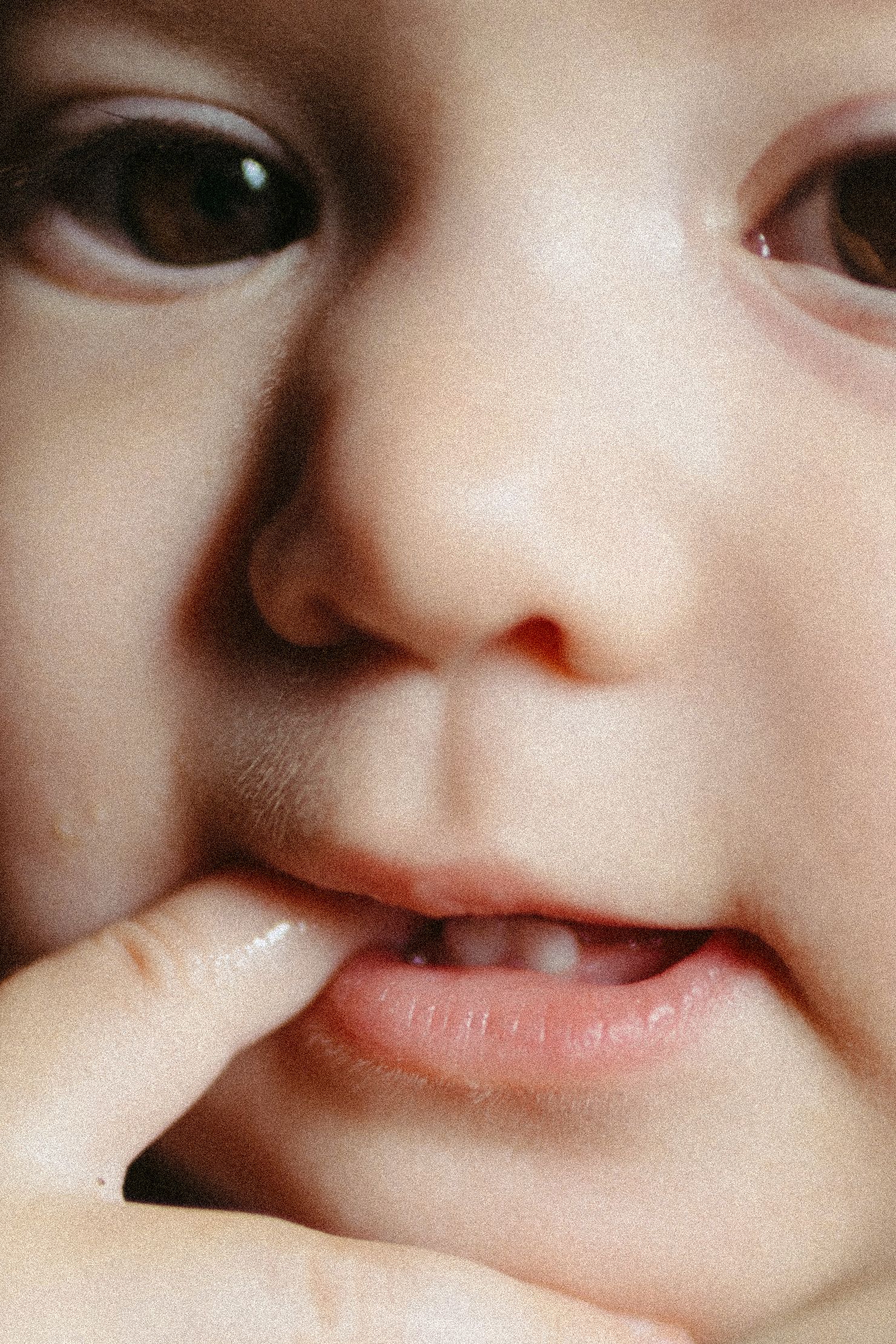 Extreme close-up of a child's face with finger touching their smiling lips.