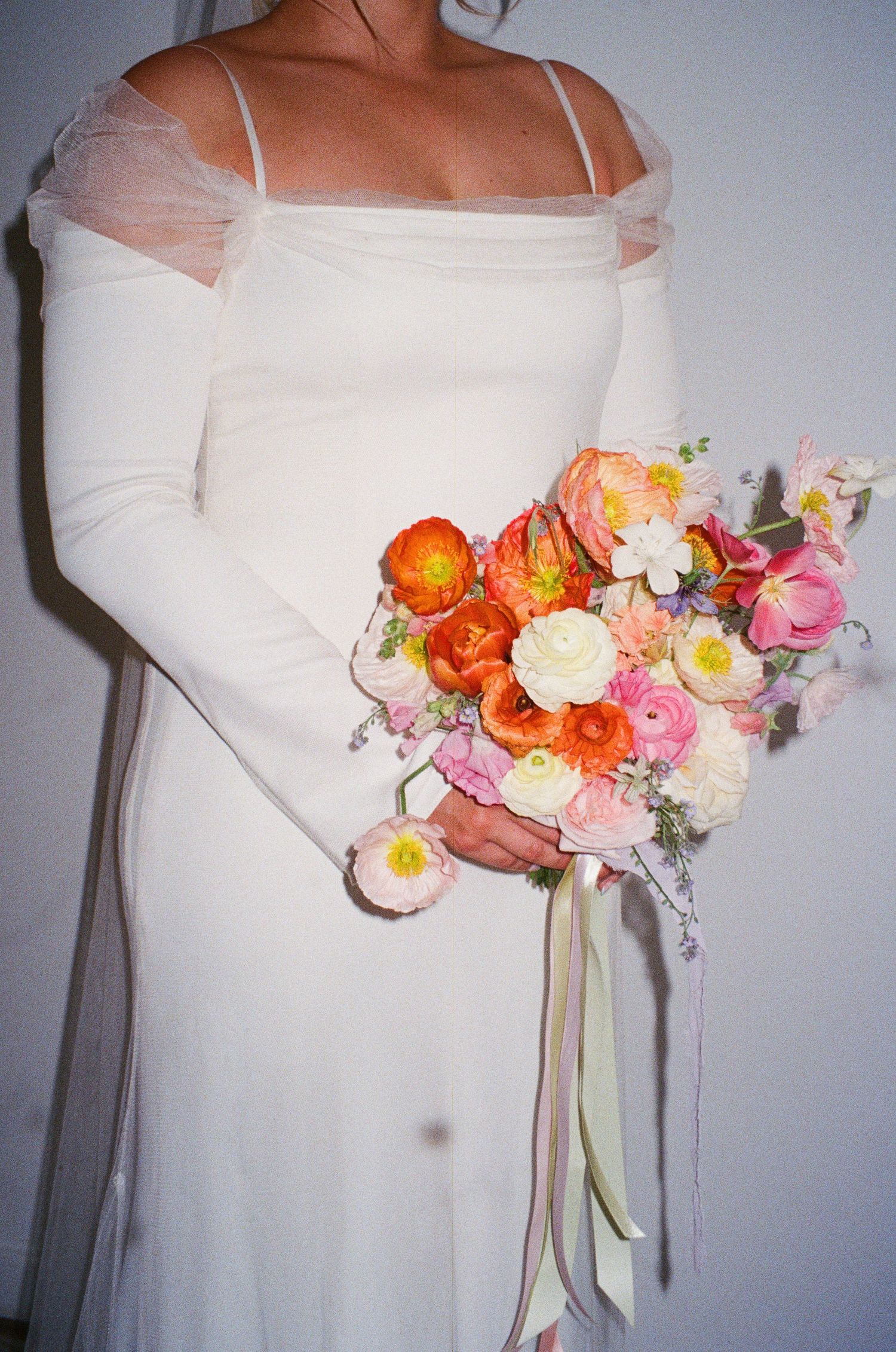 Close-up of white wedding dress and vibrant coral and pink bridal bouquet.