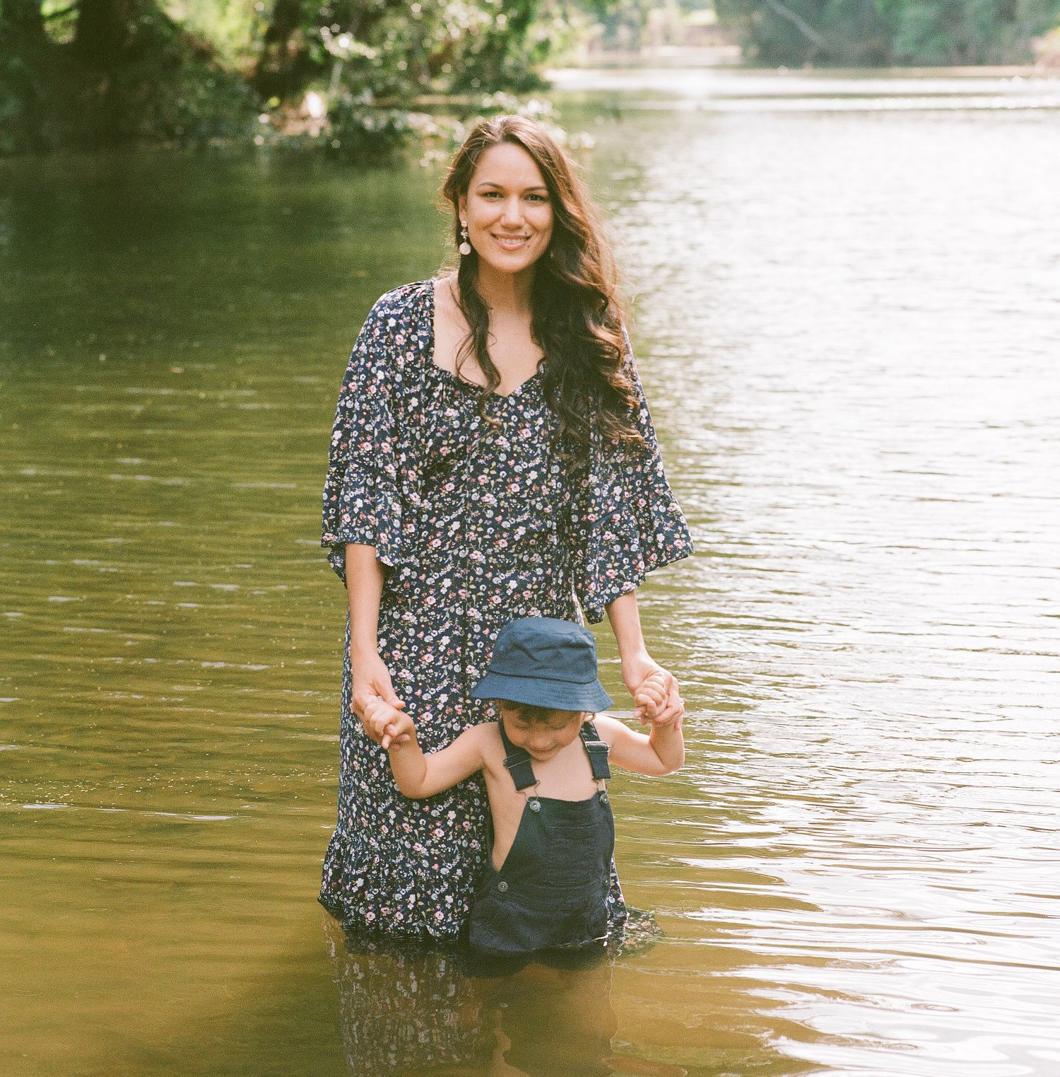 Woman in a floral dress standing in shallow water playing with someone out of frame.