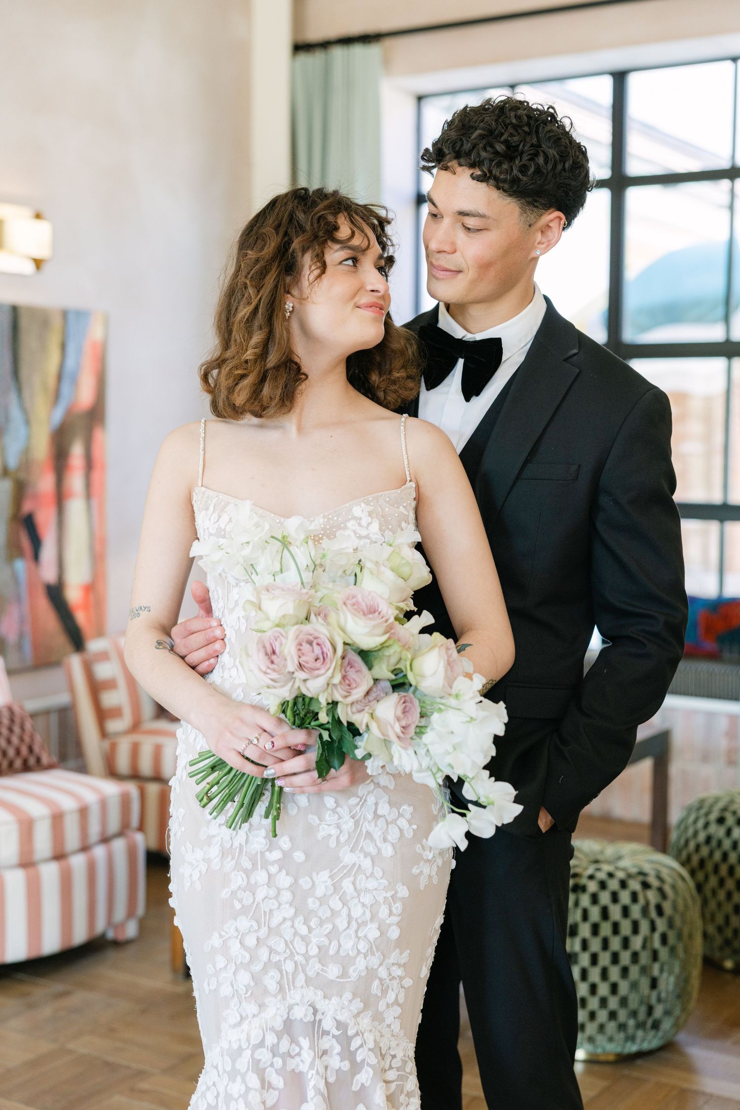 Romantic indoor wedding portrait of bride holding a pastel bouquet, standing with groom in black tuxedo - by London based Photographer
