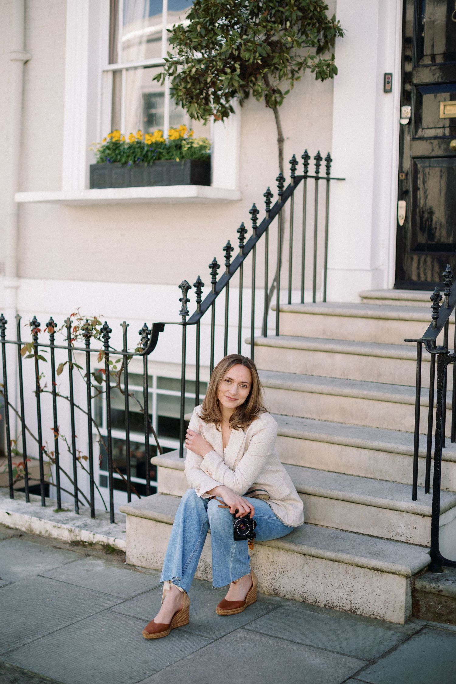 Miriam Caterina Wahl sitting on steps in front of a colourful house in Notting Hill holding her camera