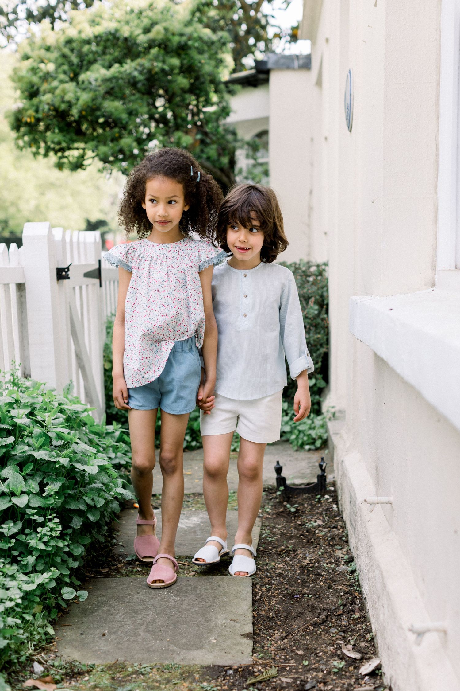 Two children holding hands in front of a white garden fence - natural family photography in London