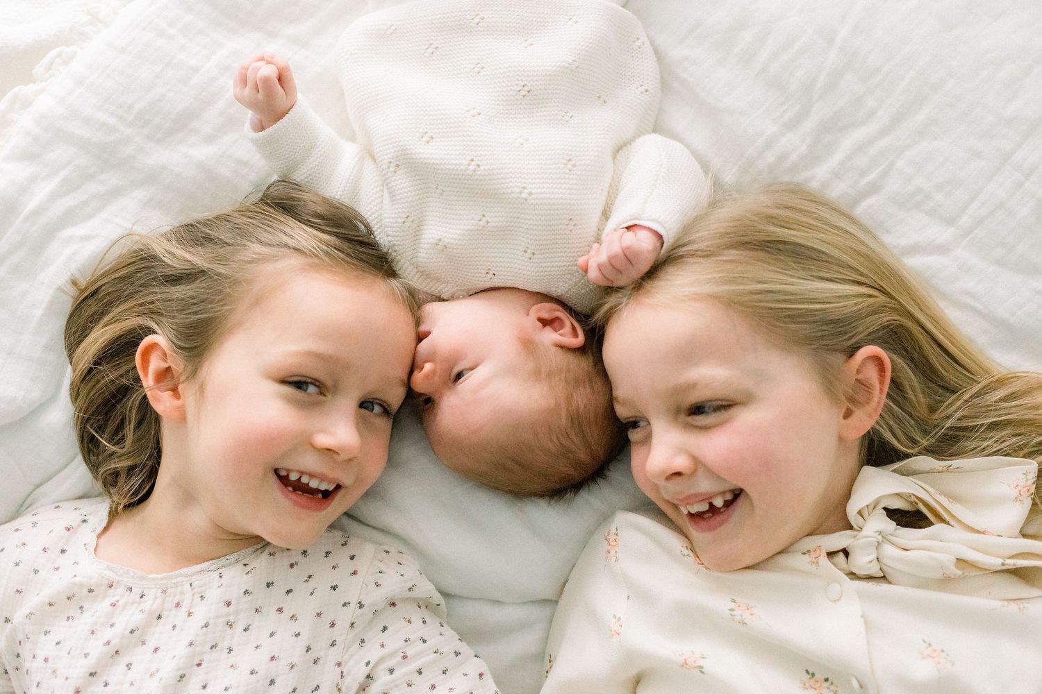 Newborn baby cuddles with his two sisters on bed