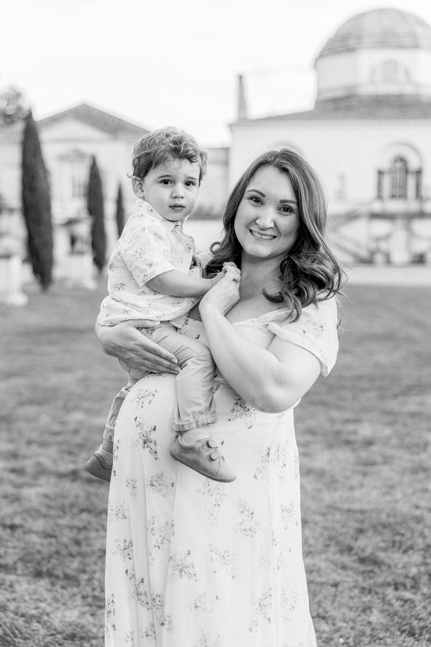pregnant woman in a flowing dress, holding her little boy in front of Chiswick House in London - fine art maternity photos london