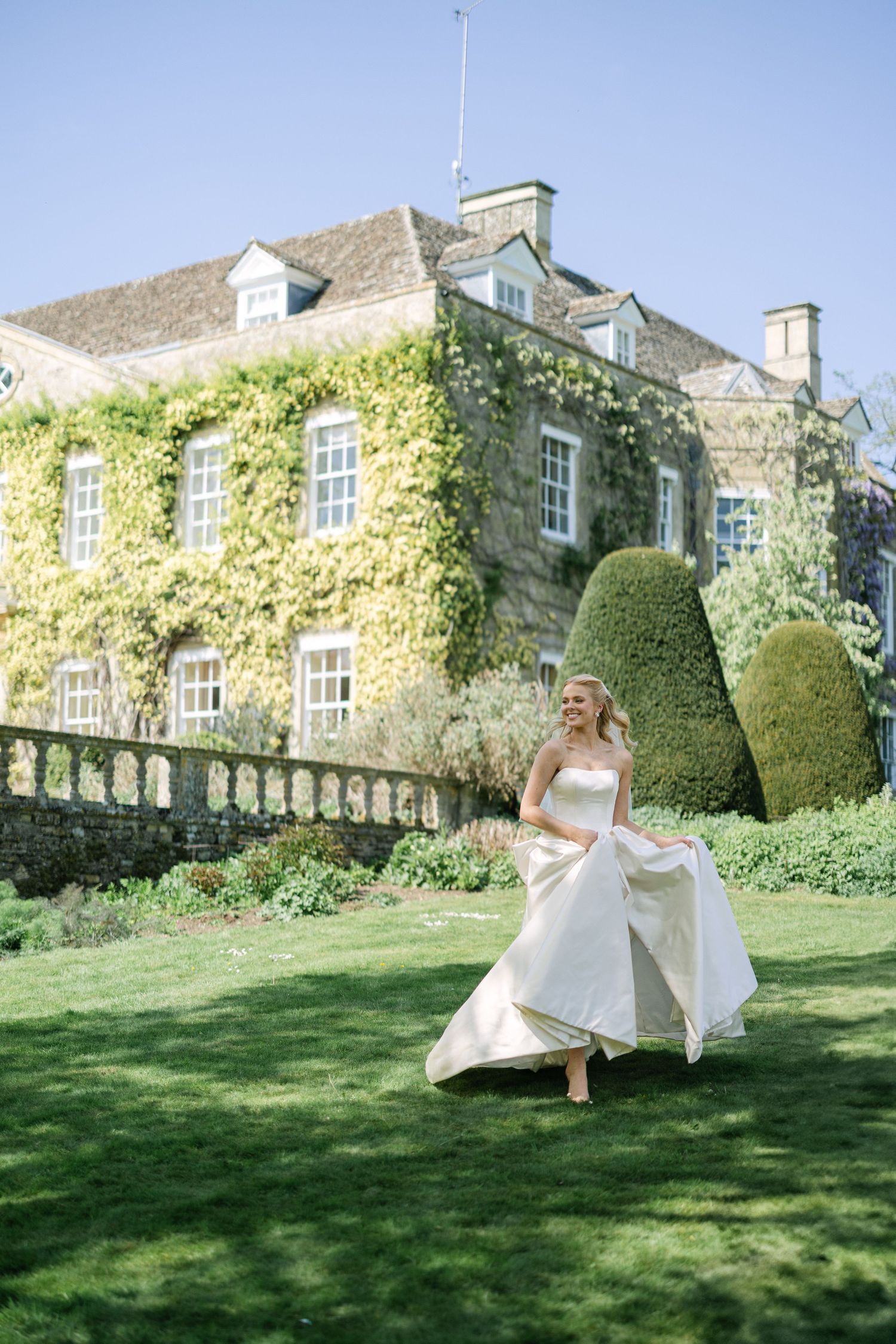 Bride running with a big smile through the picturesque gardens at the stately home Cornwell Manor - wedding photography in England