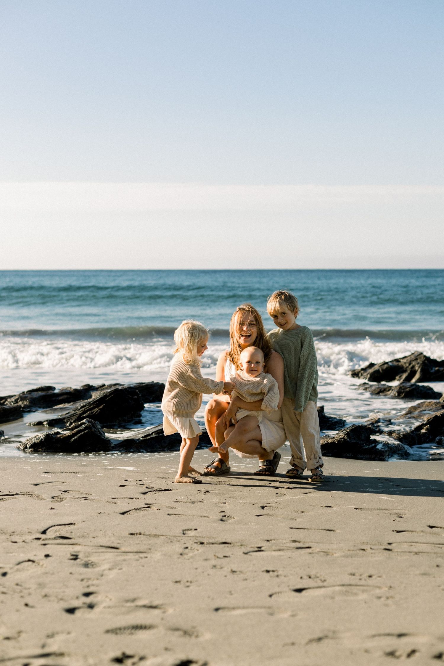 mother and her children are gold lit by the blissful morning sun in cornwall