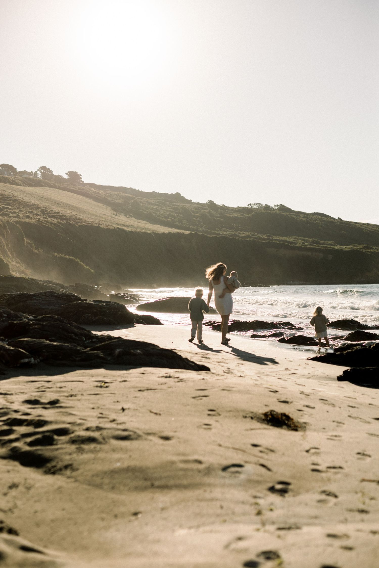 Mother an dher children walking along the beach in Cornwall with the morning sun