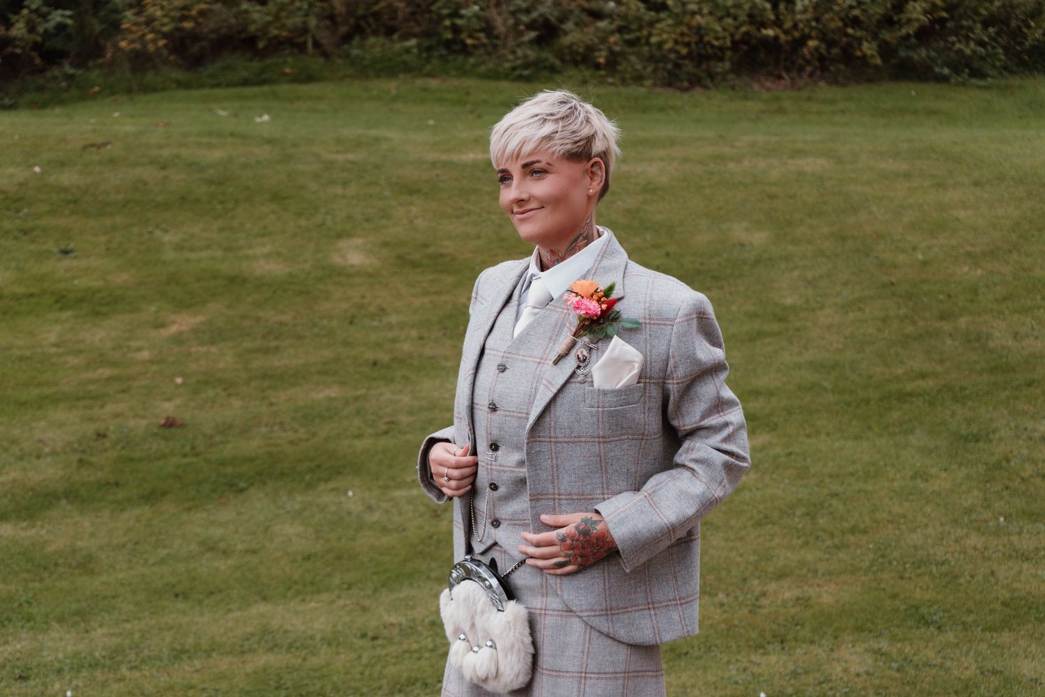 Person in grey plaid suit walking across a manicured lawn during wedding celebrations.
