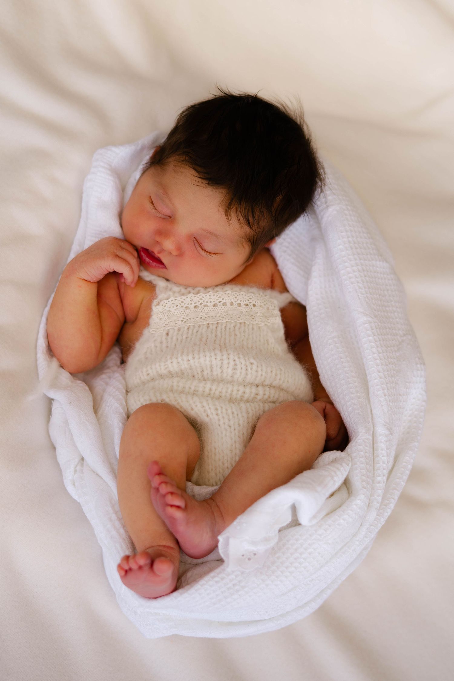 Newborn baby sleeping peacefully wrapped in white knit blanket.