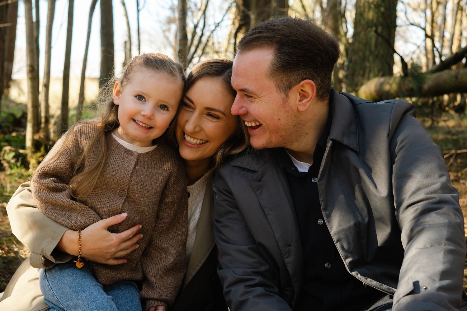 A family shares a joyful moment together in a sunlit wooded setting.