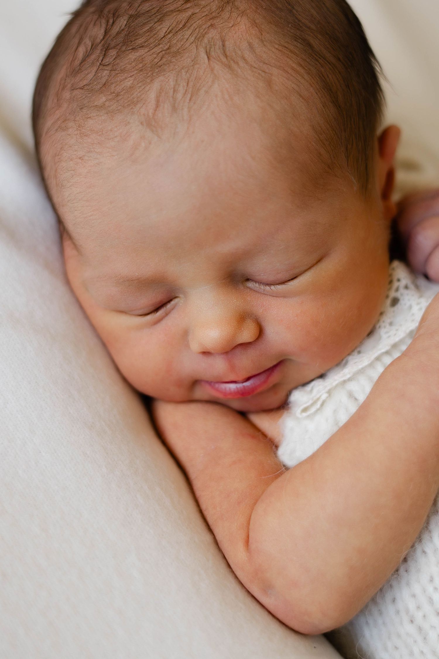 A sleeping newborn baby with peaceful expression rests on white blanket.