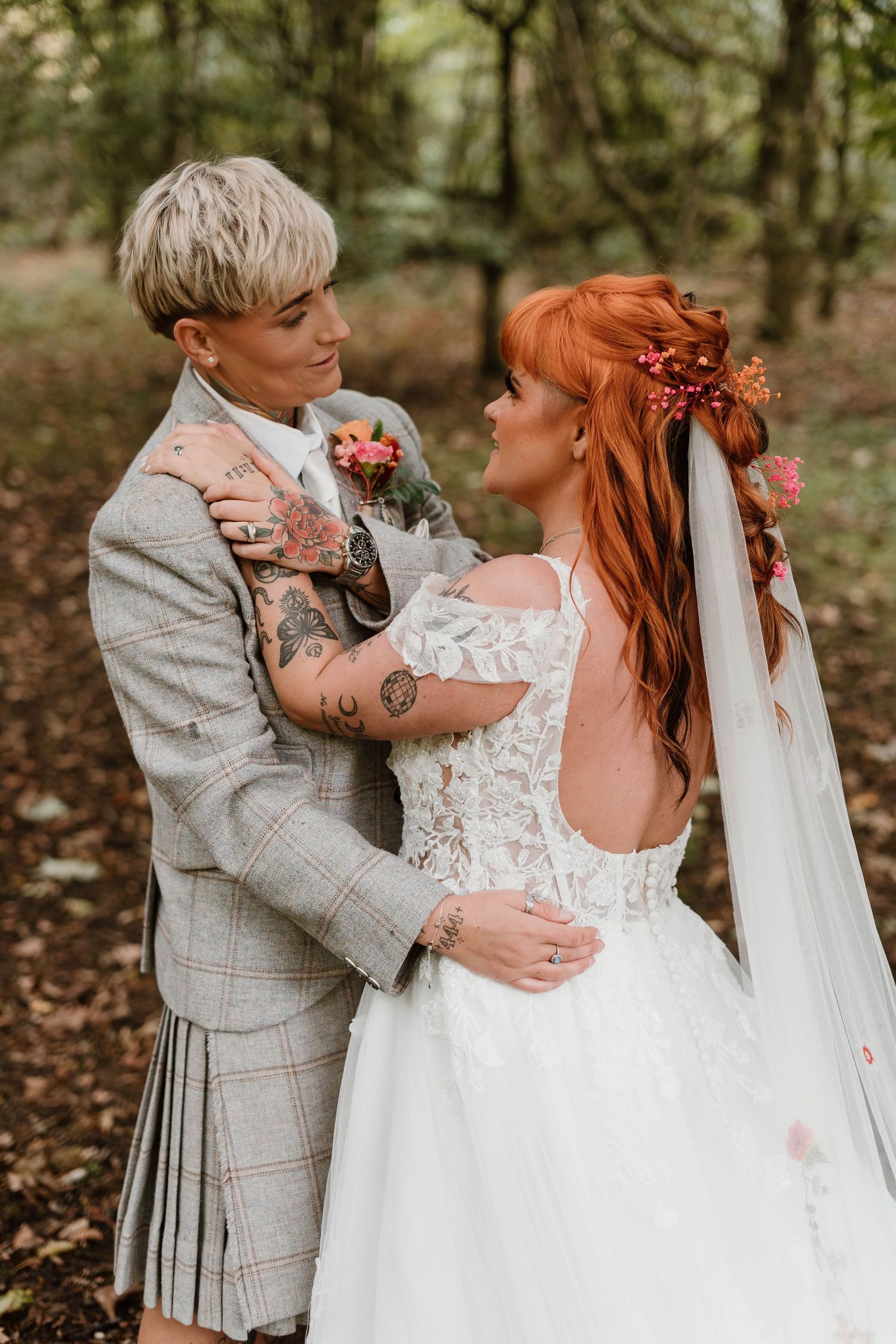 Romantic autumn wedding couple embracing in a wooded setting with fallen leaves.