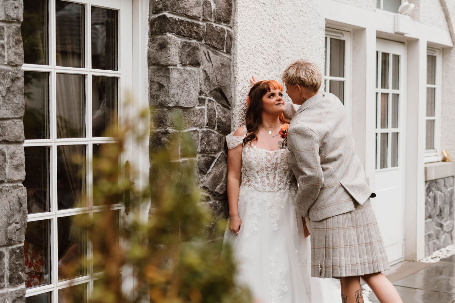 Wedding couple shares intimate moments against white stone building wall.