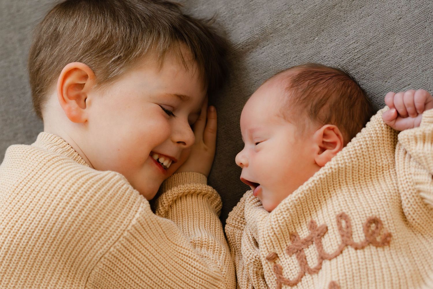 Heartwarming sibling bonding moment with newborn baby on neutral bedding.