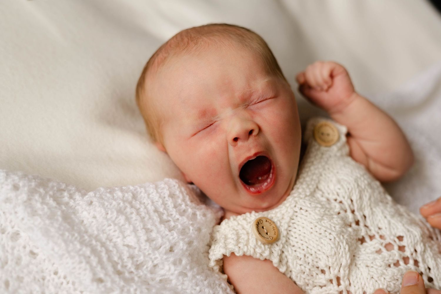 Close up of sleeping newborn baby wearing delicate white lace dress.
