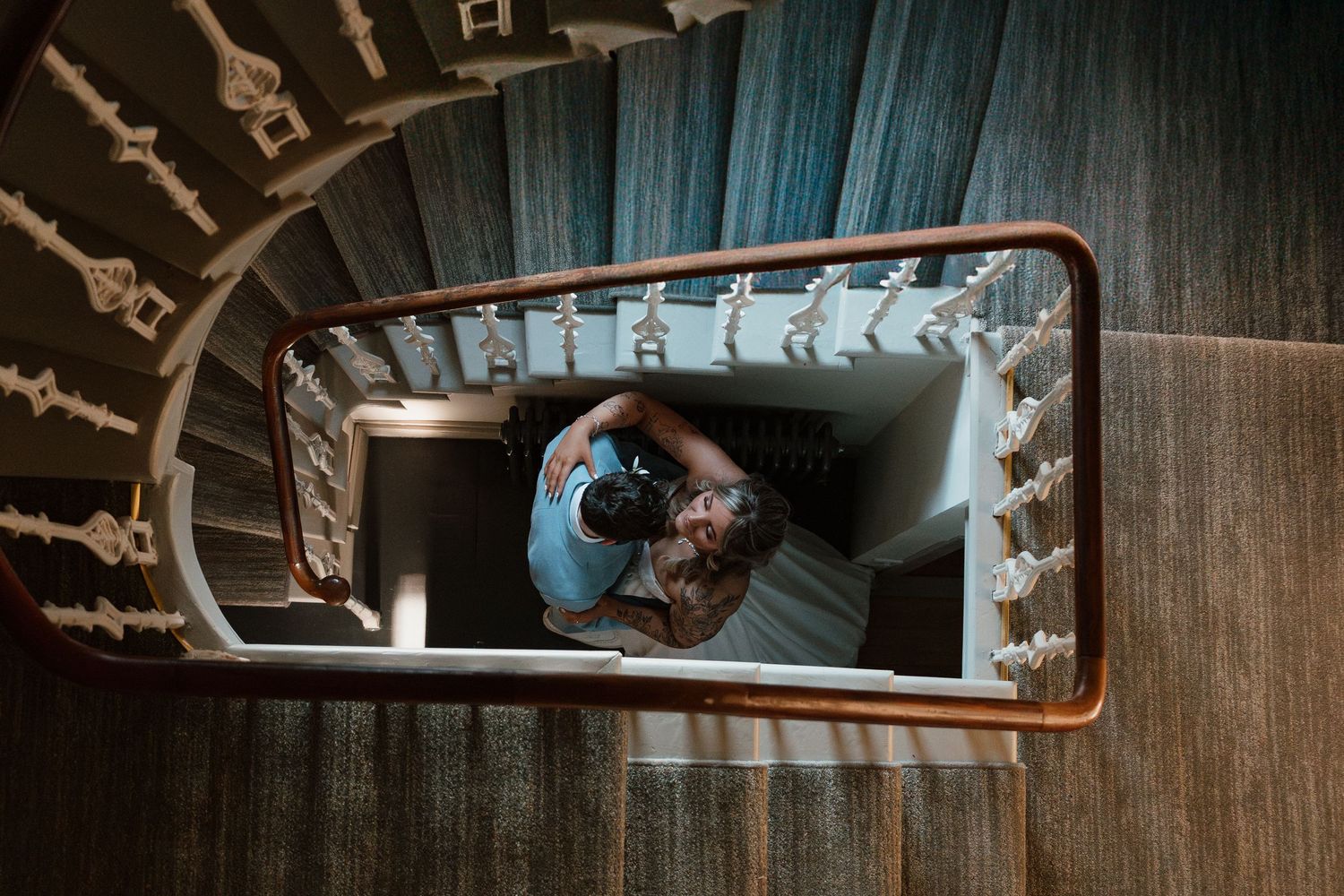 Aerial view of a person standing in a spiral staircase with wooden railings and patterned carpet.