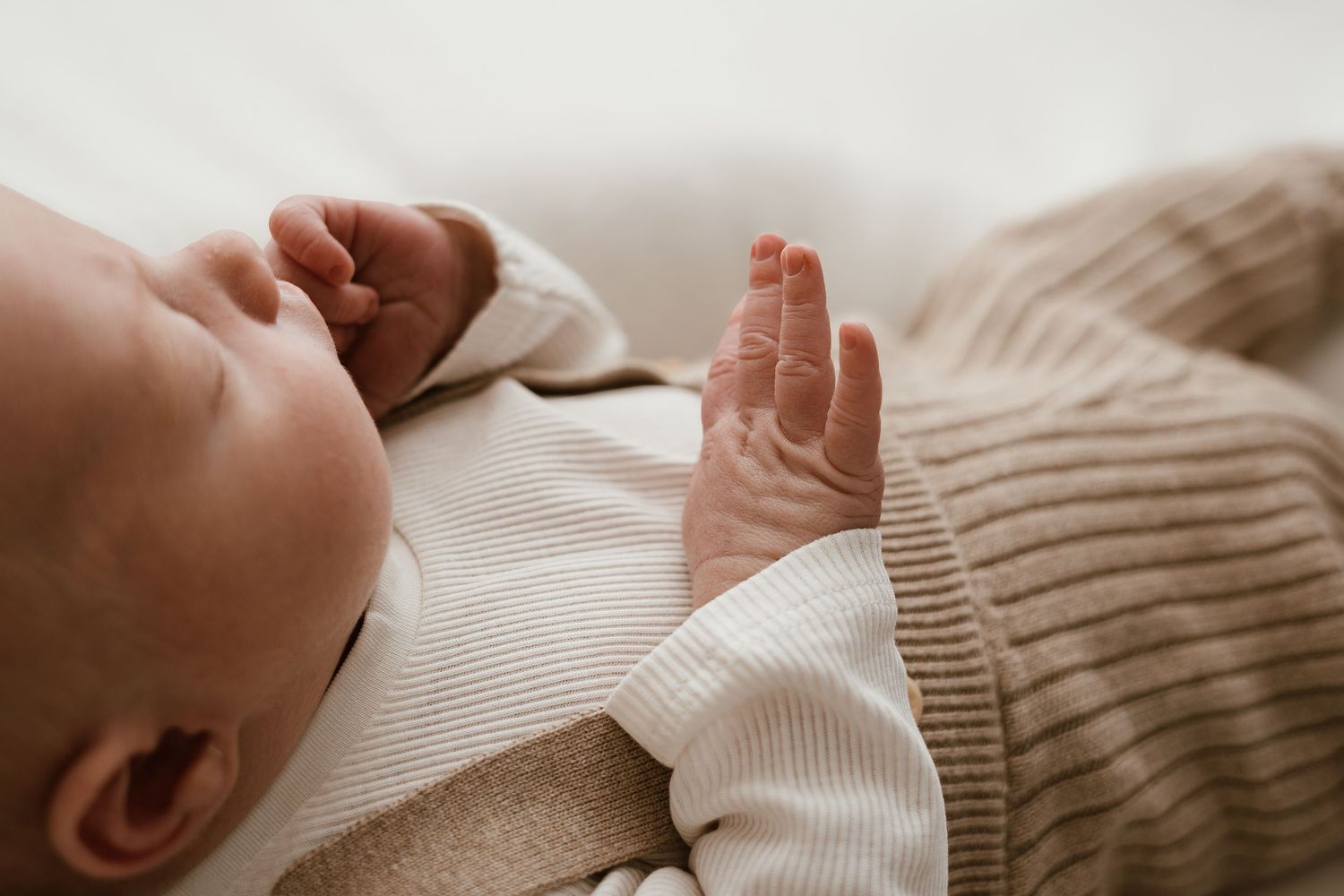 Close-up of a peaceful newborn baby lying down, wearing a striped onesie, with tiny fingers spread open.