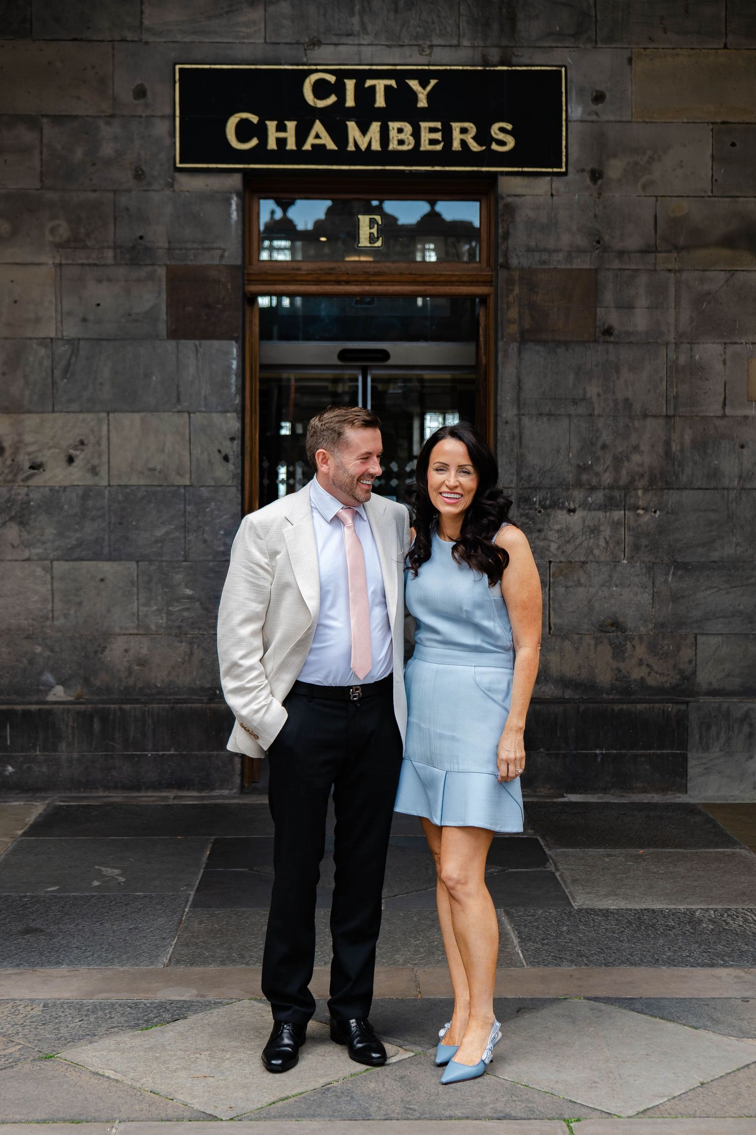 Couple poses playfully outside City Chambers building entrance.