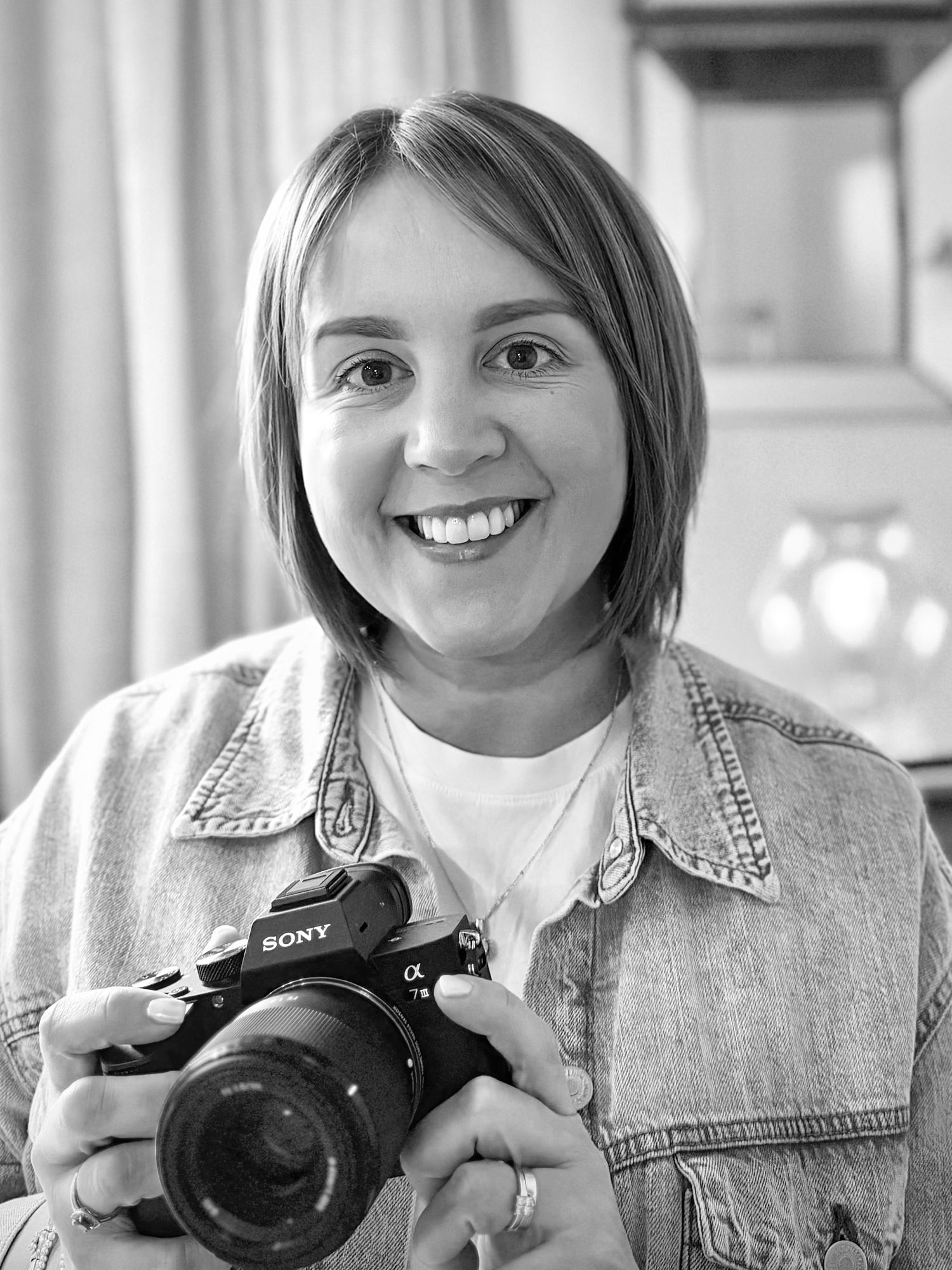 Black and white portrait of a photographer holding a Sony camera while wearing a denim jacket and white shirt.
