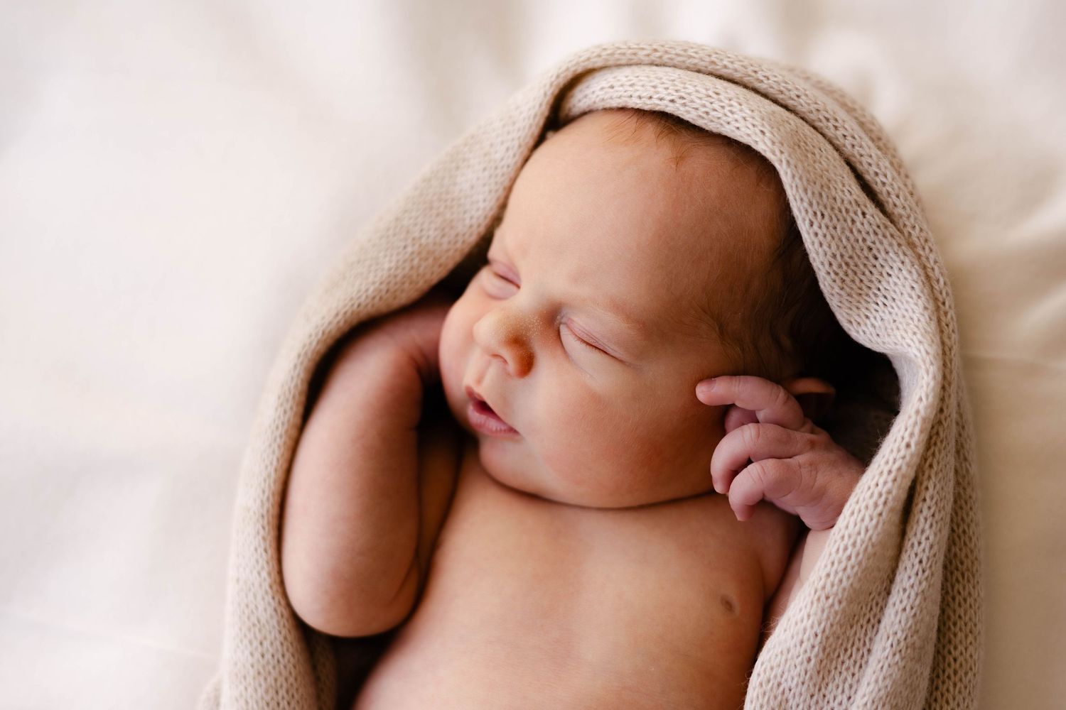 Artistic newborn portrait series showing baby wrapped in soft beige blanket.