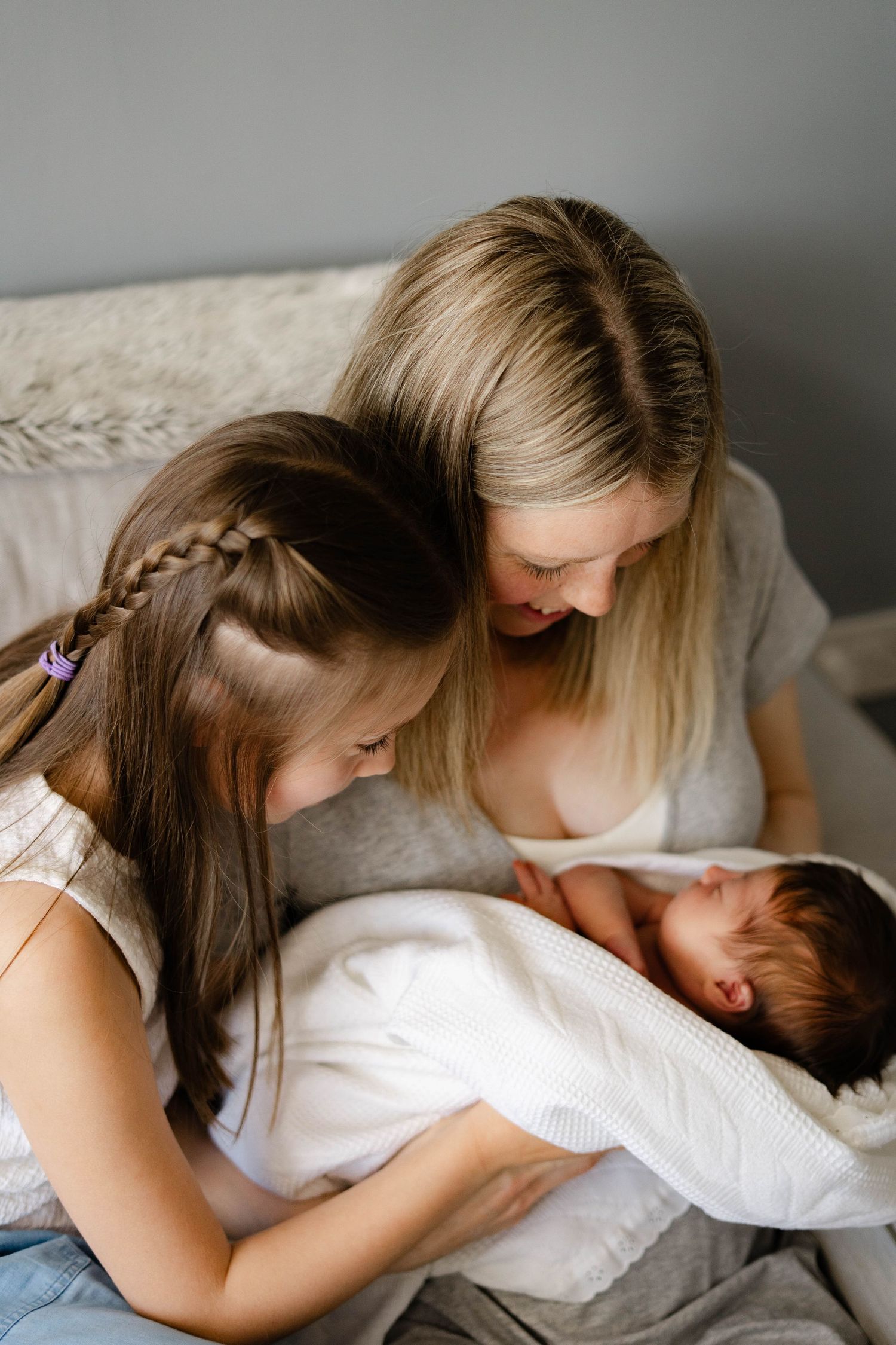 Tender family moment during newborn photo session on gray bedding.
