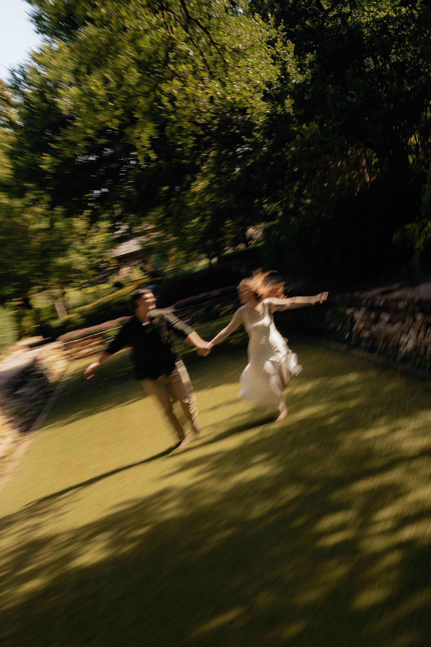 Blurred motion photo of a bride and groom running hand in hand across a lush green lawn on their wedding day.