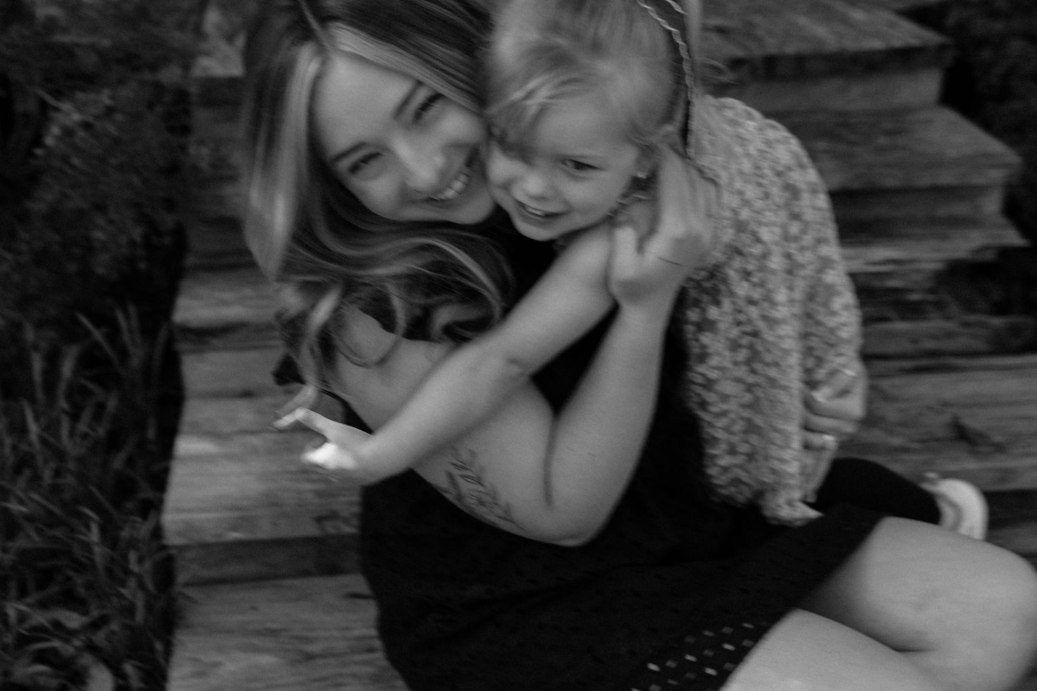 Black and white photo of a smiling woman hugging a young child on outdoor steps.
