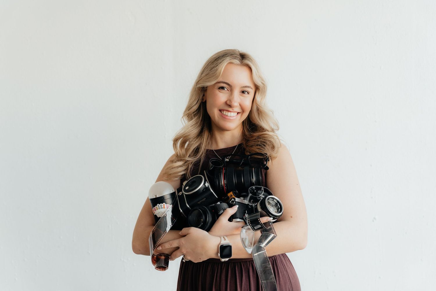 Professional photographer with blonde hair holds camera equipment against white studio backdrop.