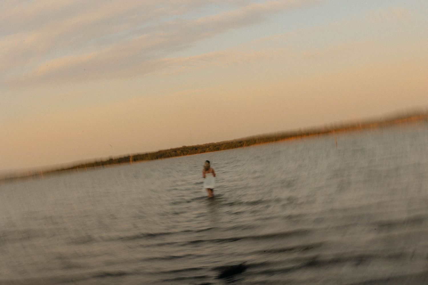 Distant figure walks along a calm waterfront during sunset.