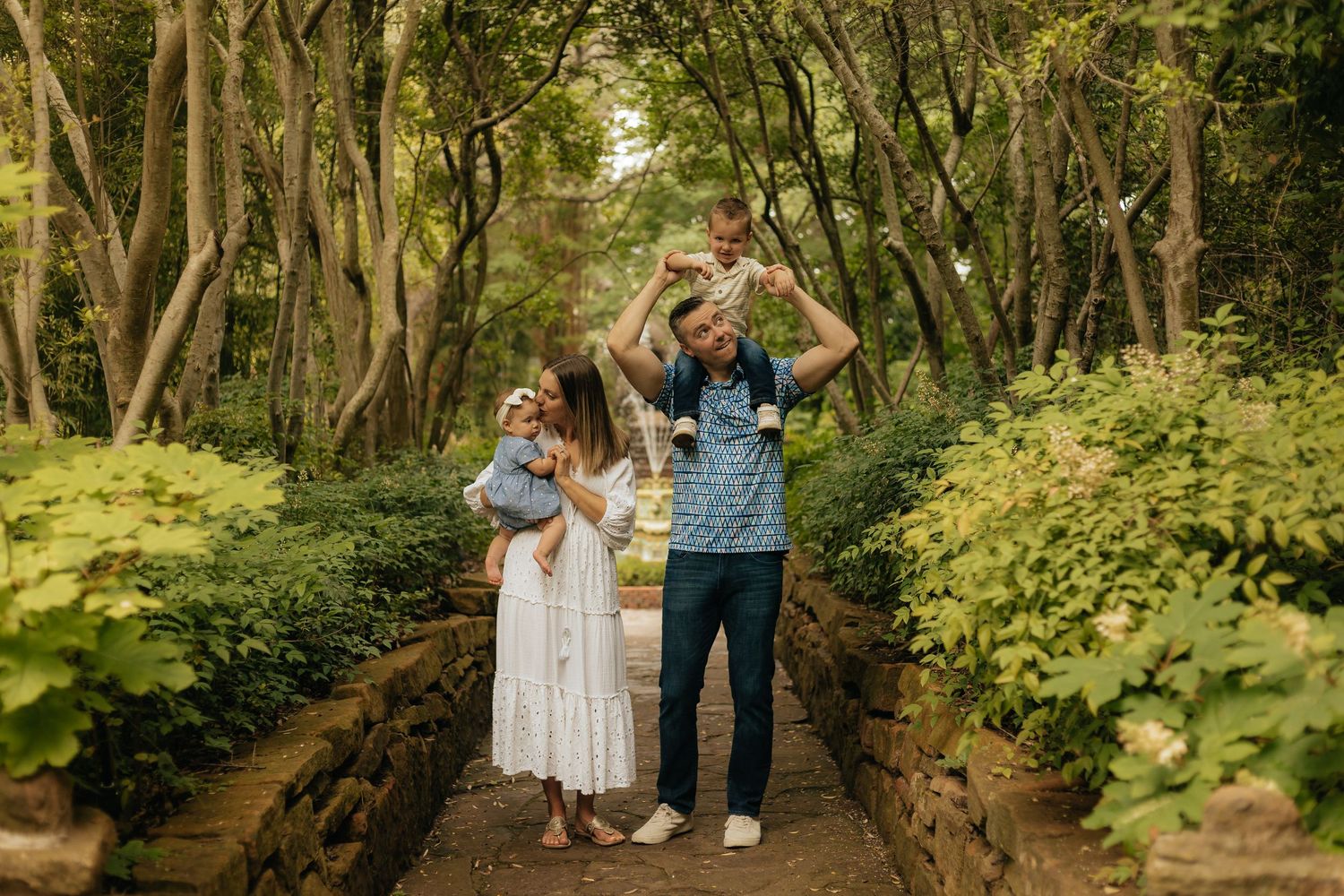 Family having fun walking on a wooden bridge in a lush green forest setting.