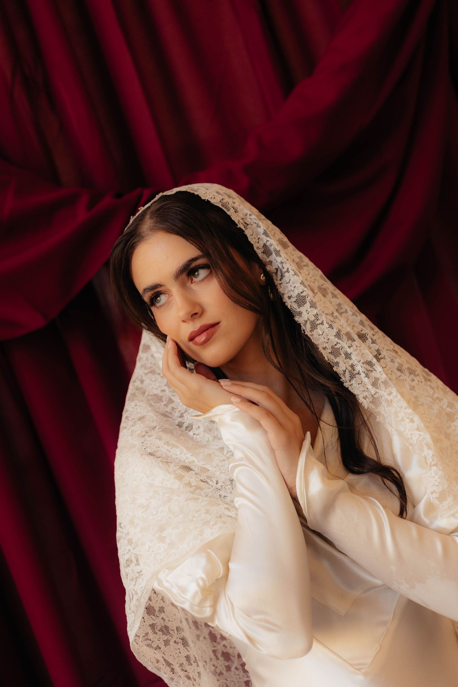 Ethereal bridal portrait featuring lace sleeves against burgundy velvet backdrop.